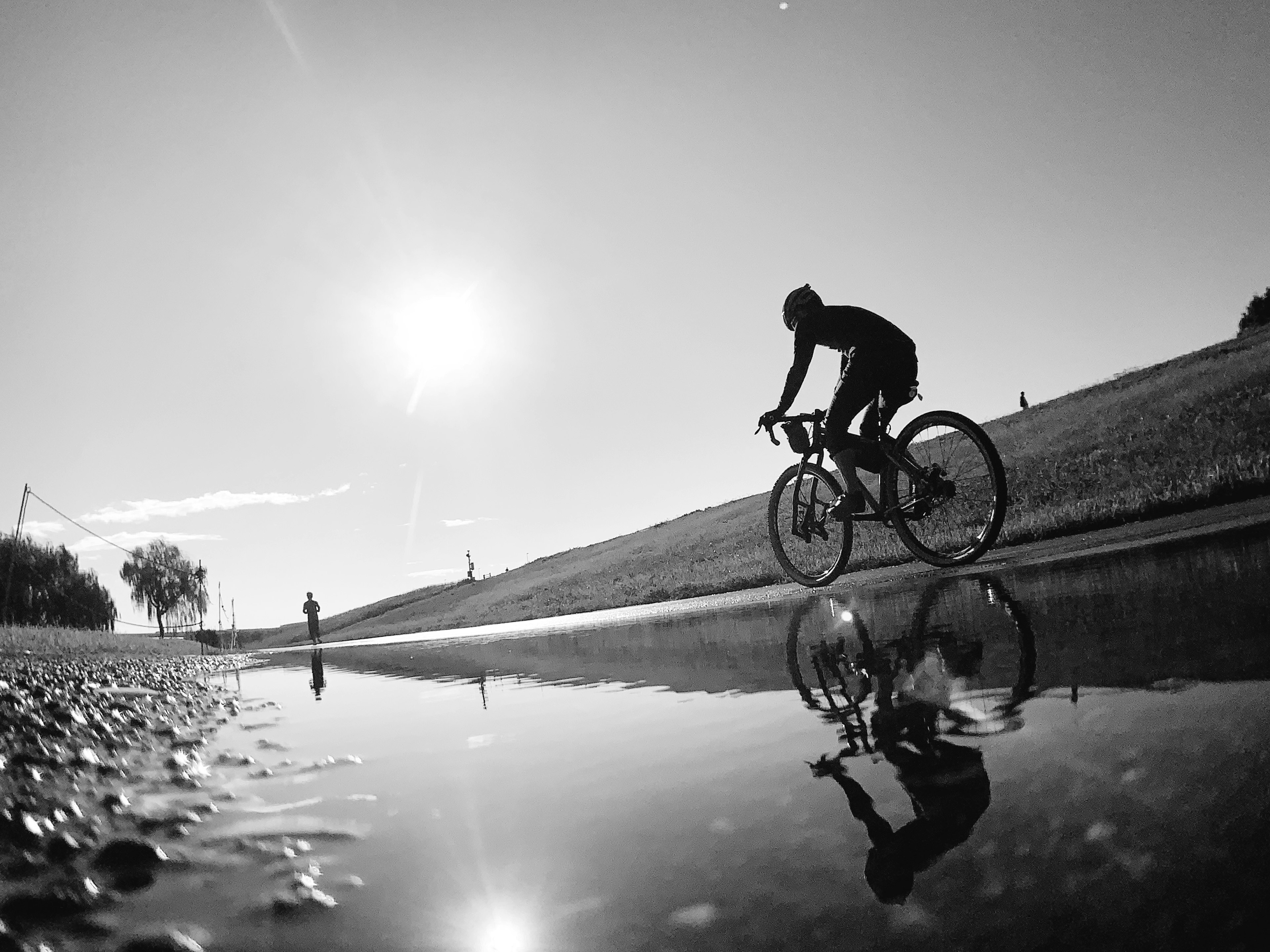 Ein Radfahrer, der entlang eines Weges mit einem Spiegelbild in einer Pfütze in Schwarzweiß fährt