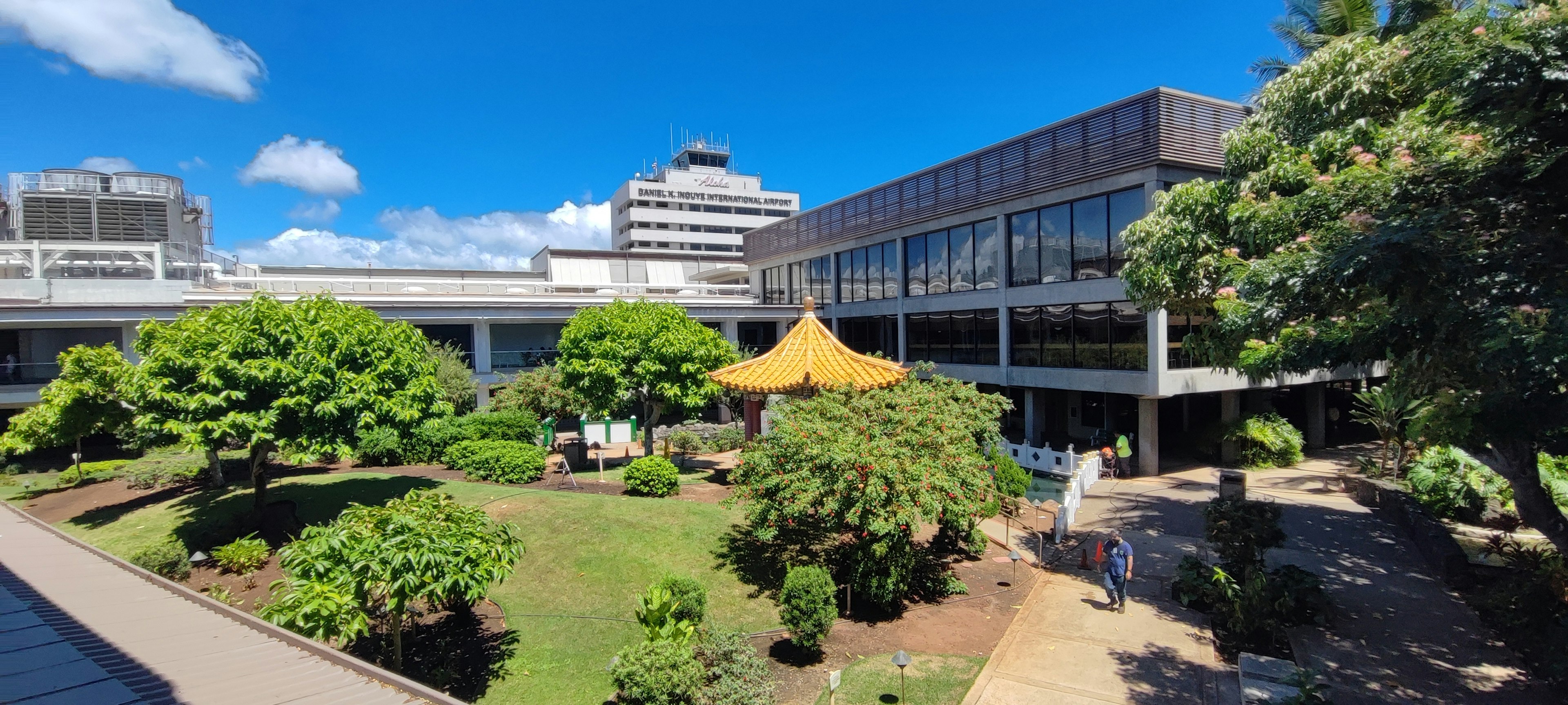 Un jardín vibrante con árboles y una carpa amarilla bajo un cielo azul