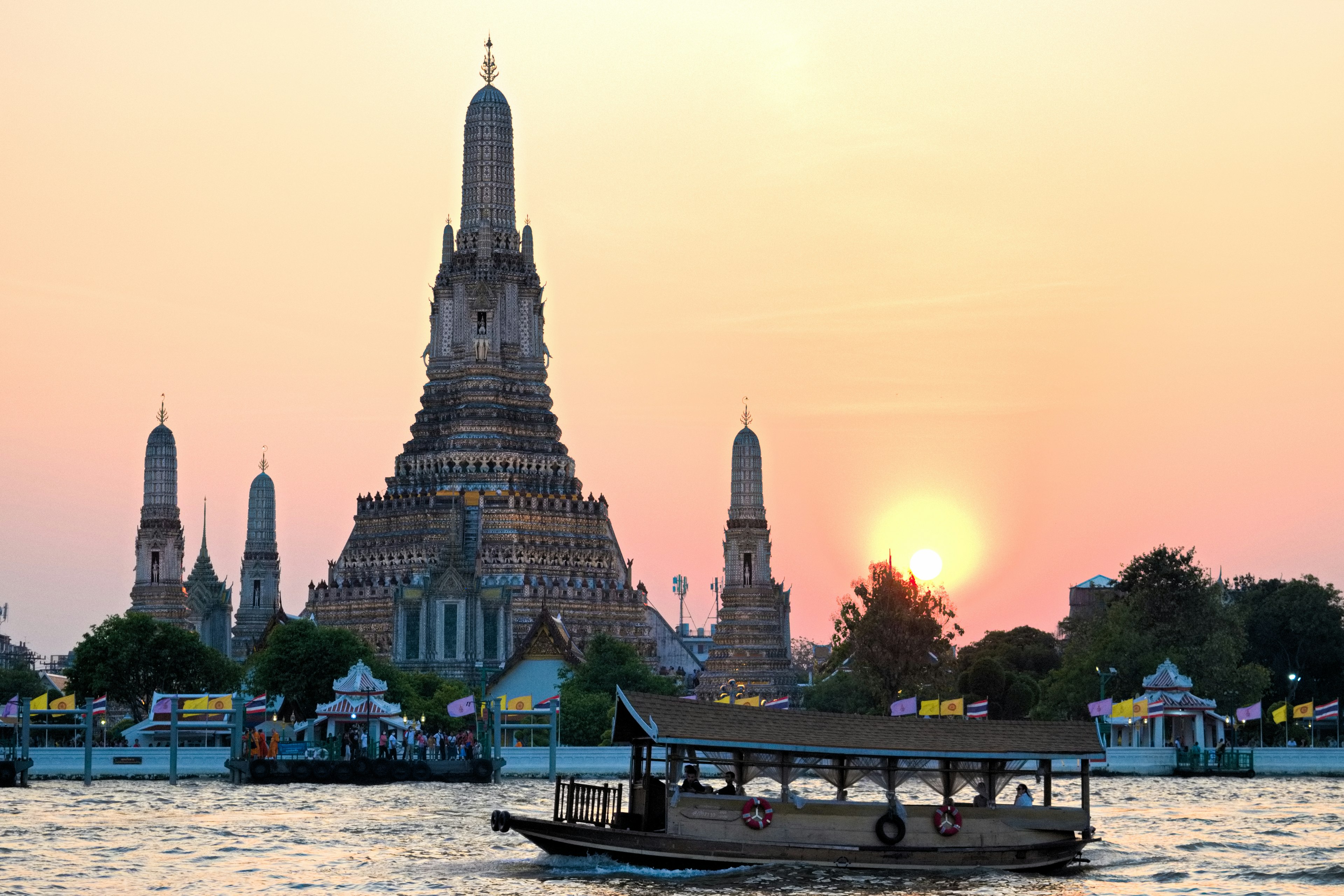 Kuil Wat Arun dengan latar belakang matahari terbenam dan perahu di sungai