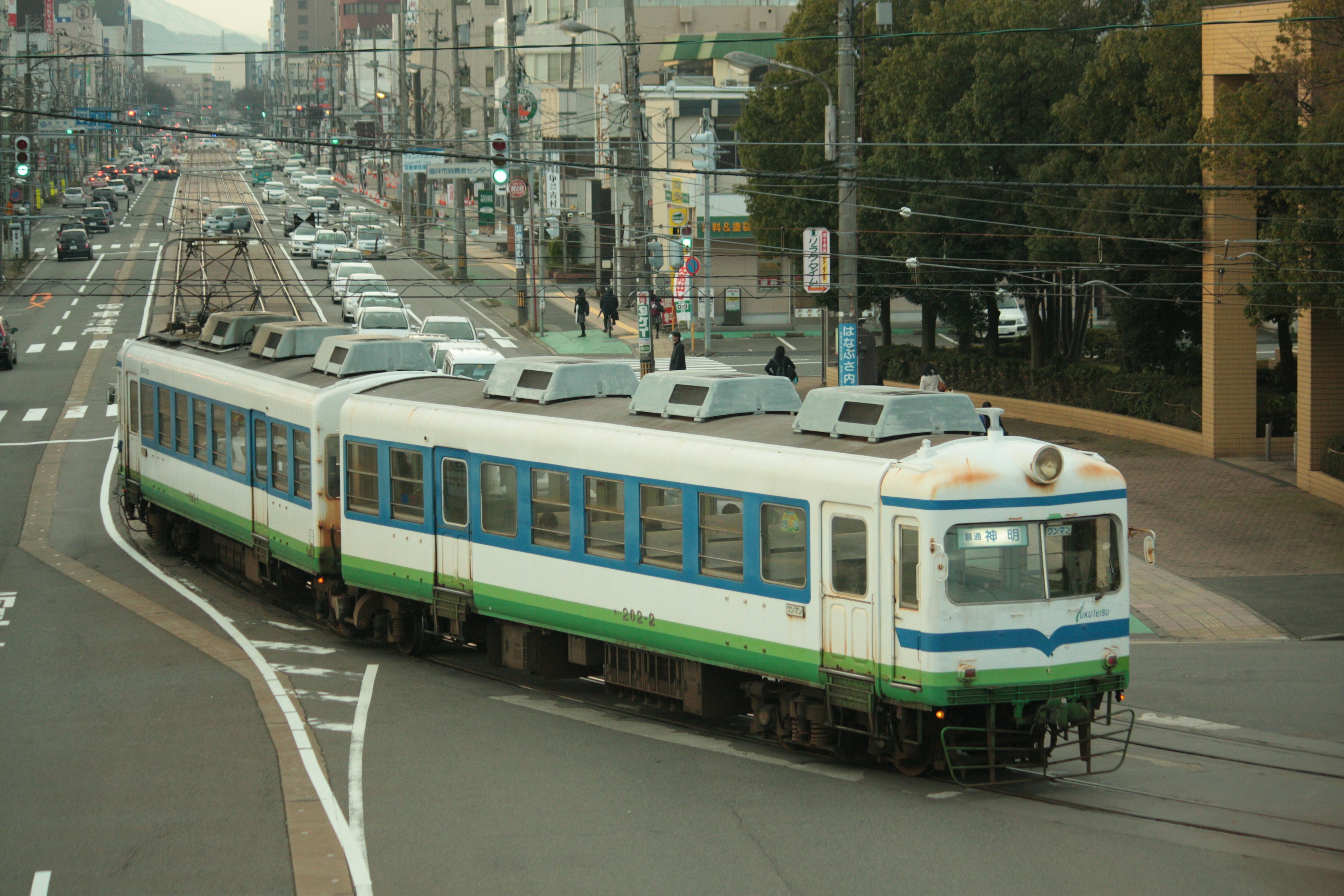 青と緑のストライプの電車が曲がり角を曲がるシーン