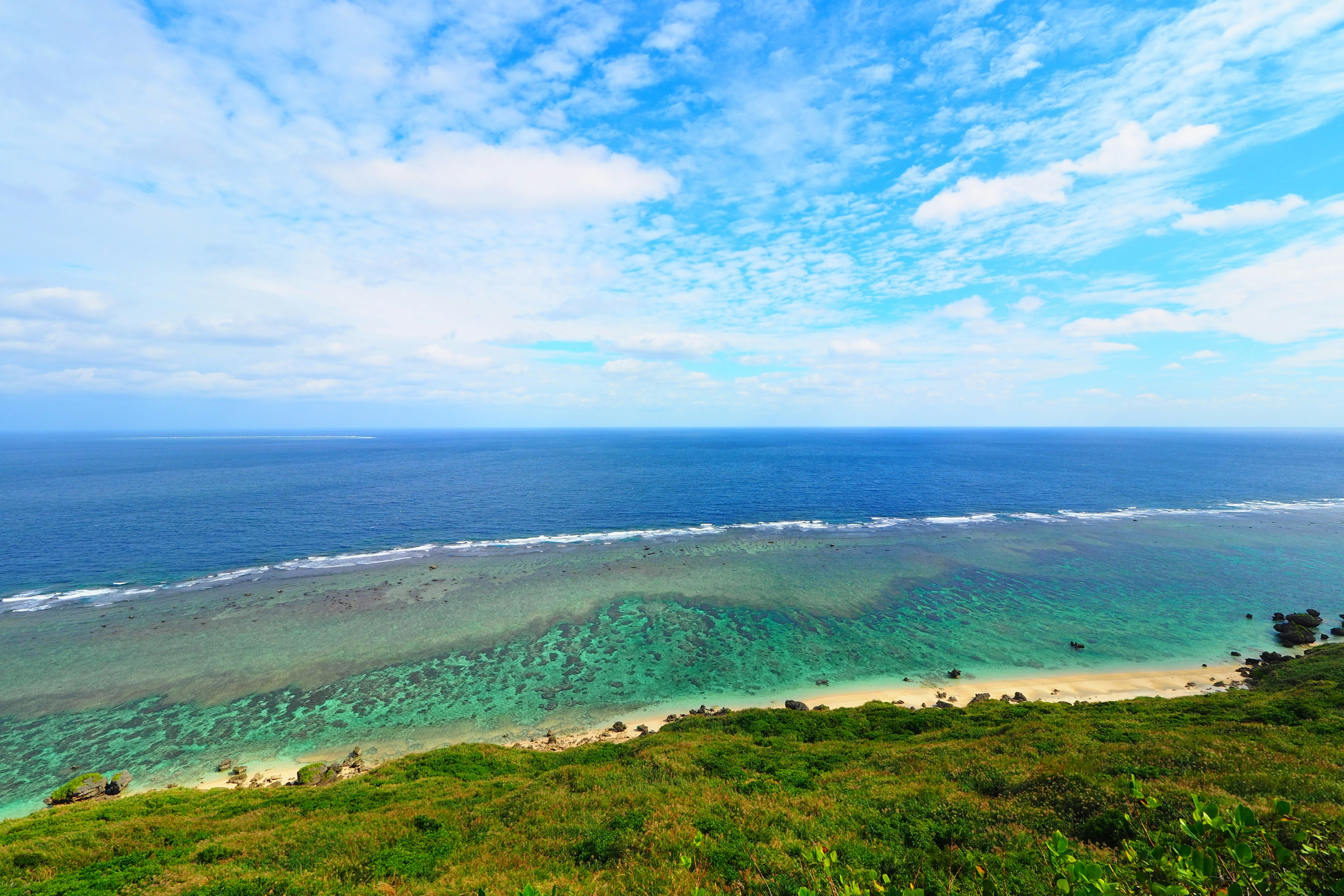 Pemandangan indah laut dan langit biru dengan rumput hijau dan terumbu karang terlihat