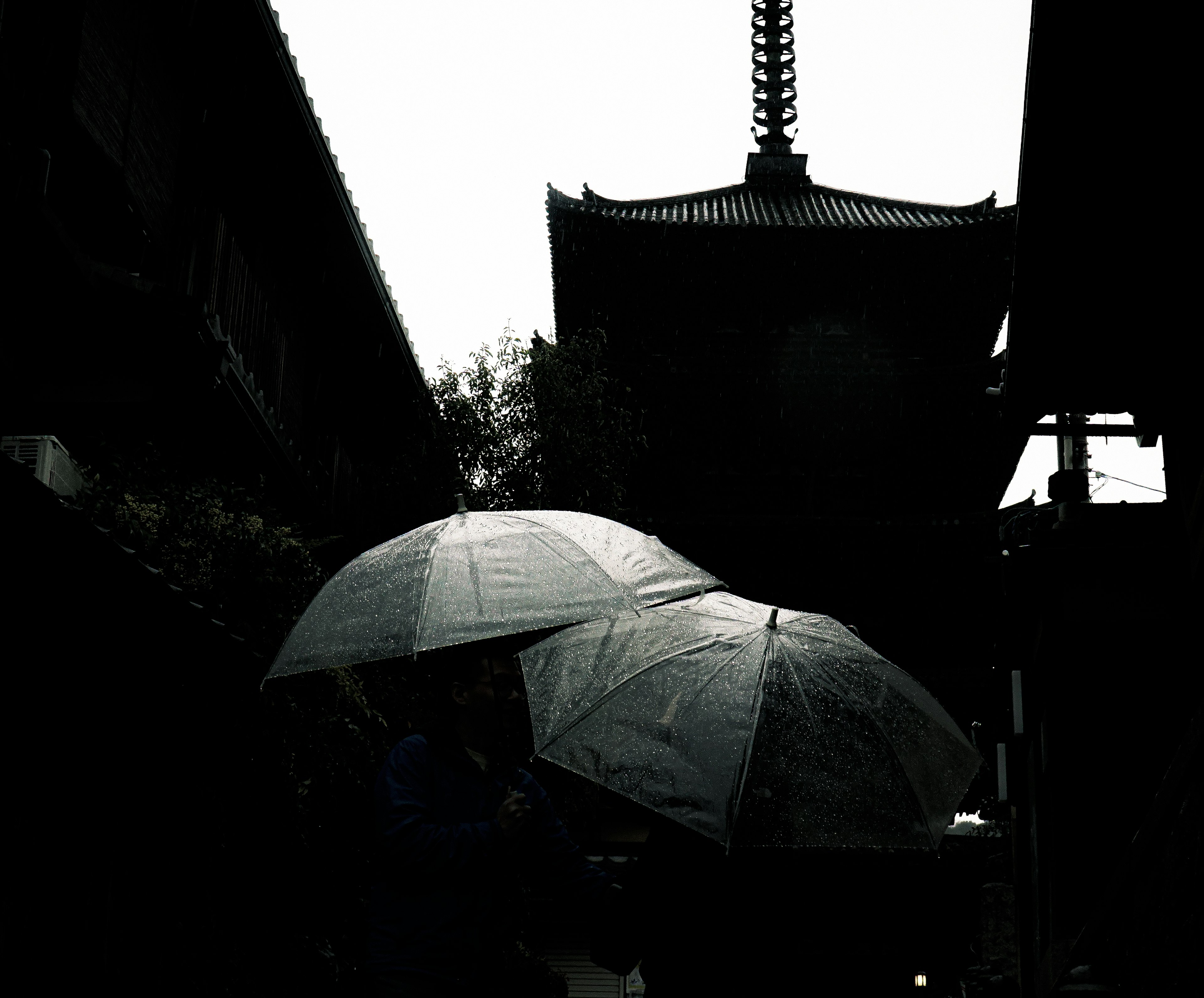 Dark scene highlighting people with umbrellas and a pagoda in the background