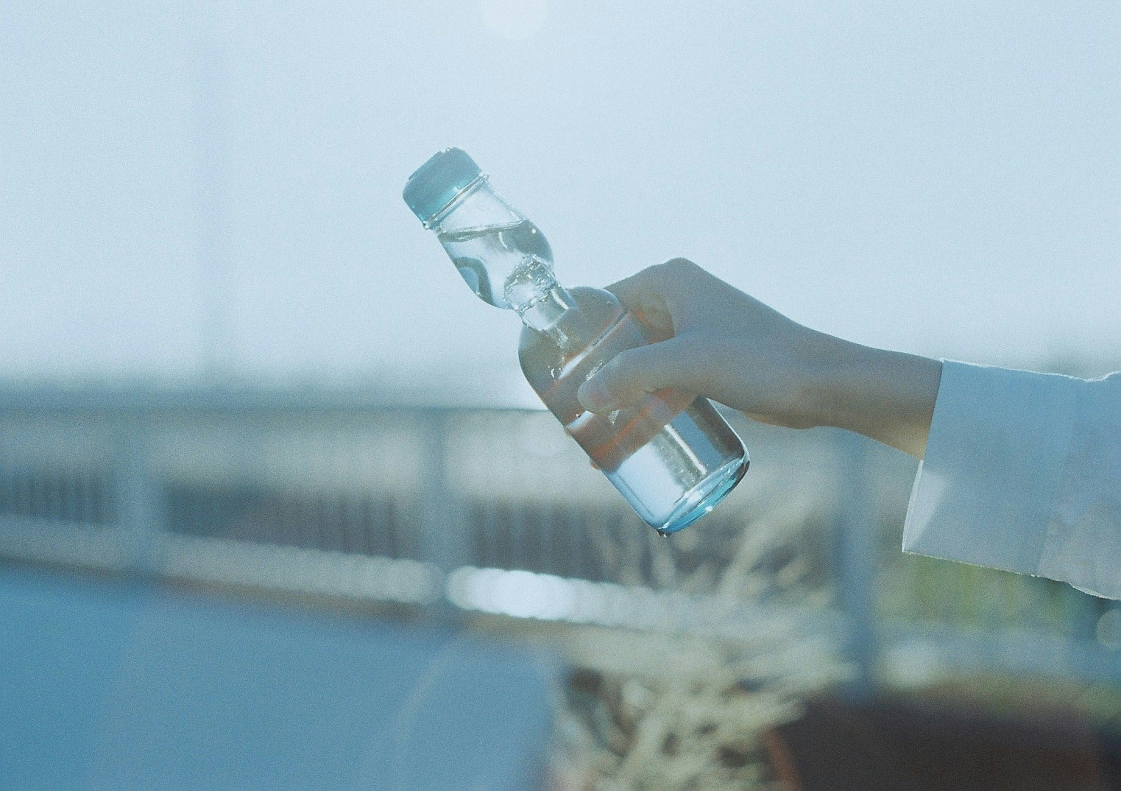 Primer plano de una mano sosteniendo una botella de agua clara bajo un cielo azul