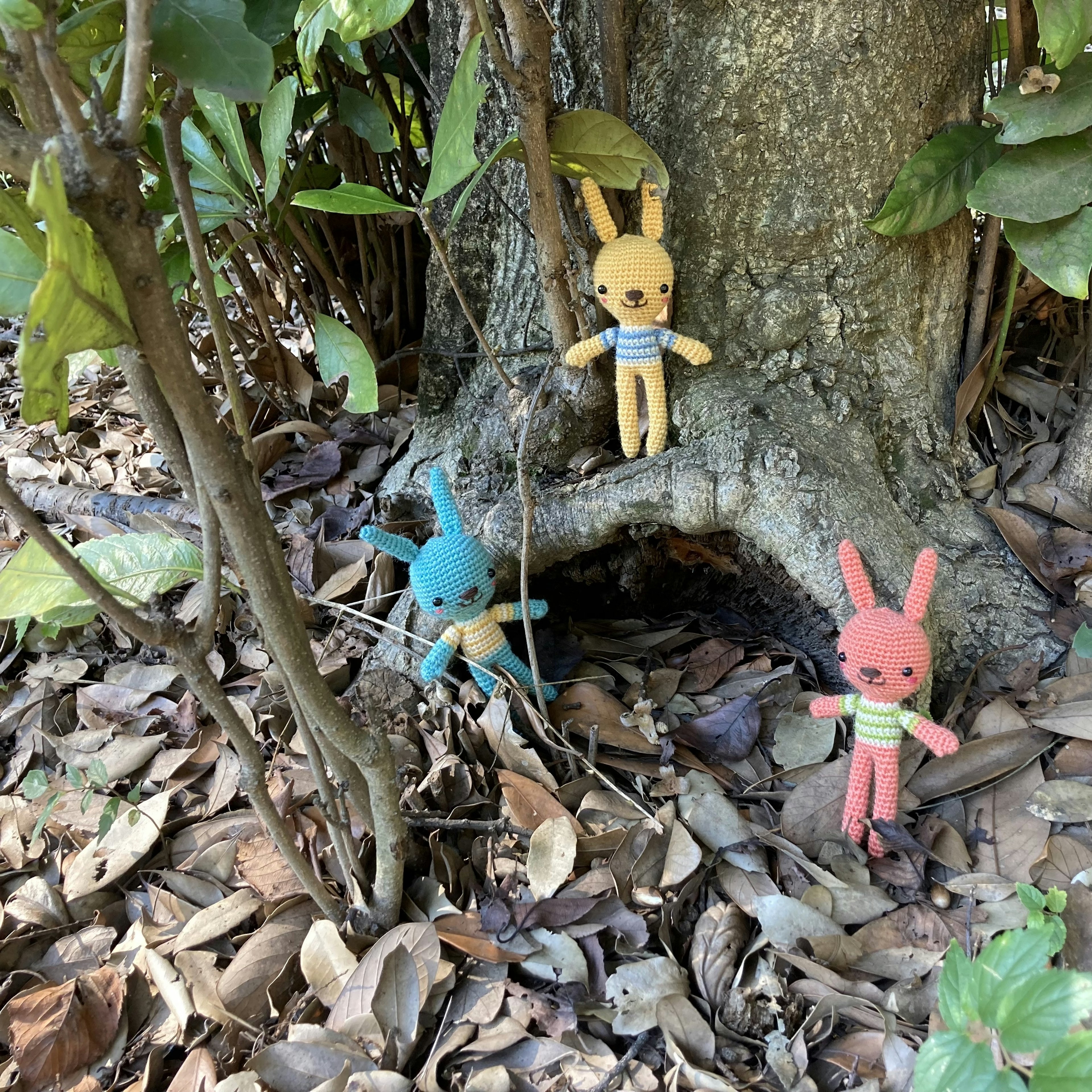 Juguetes de peluche coloridos de conejitos junto a un árbol