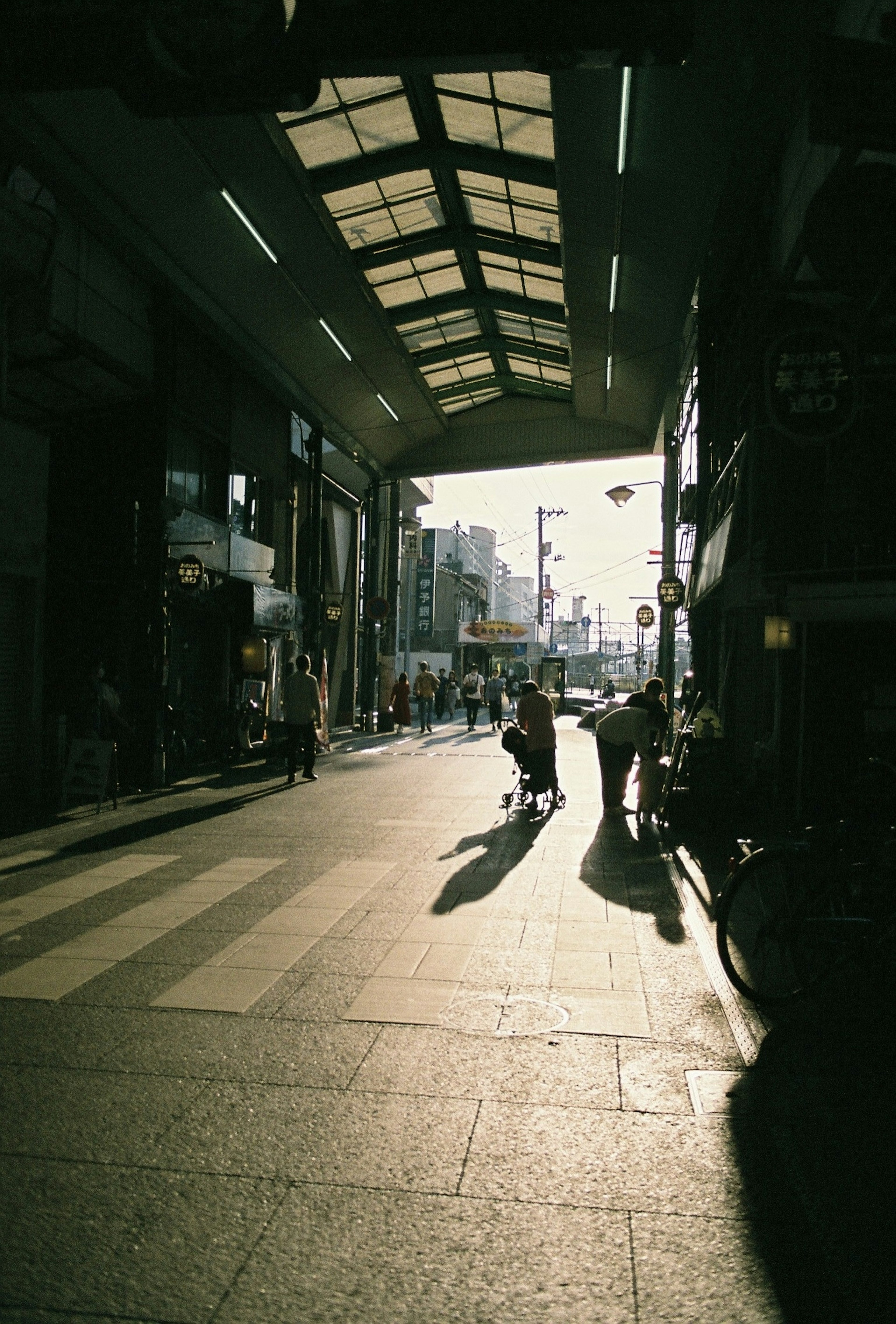 人々が歩いている商業地区の通りで、夕暮れ時の影が長く伸びている