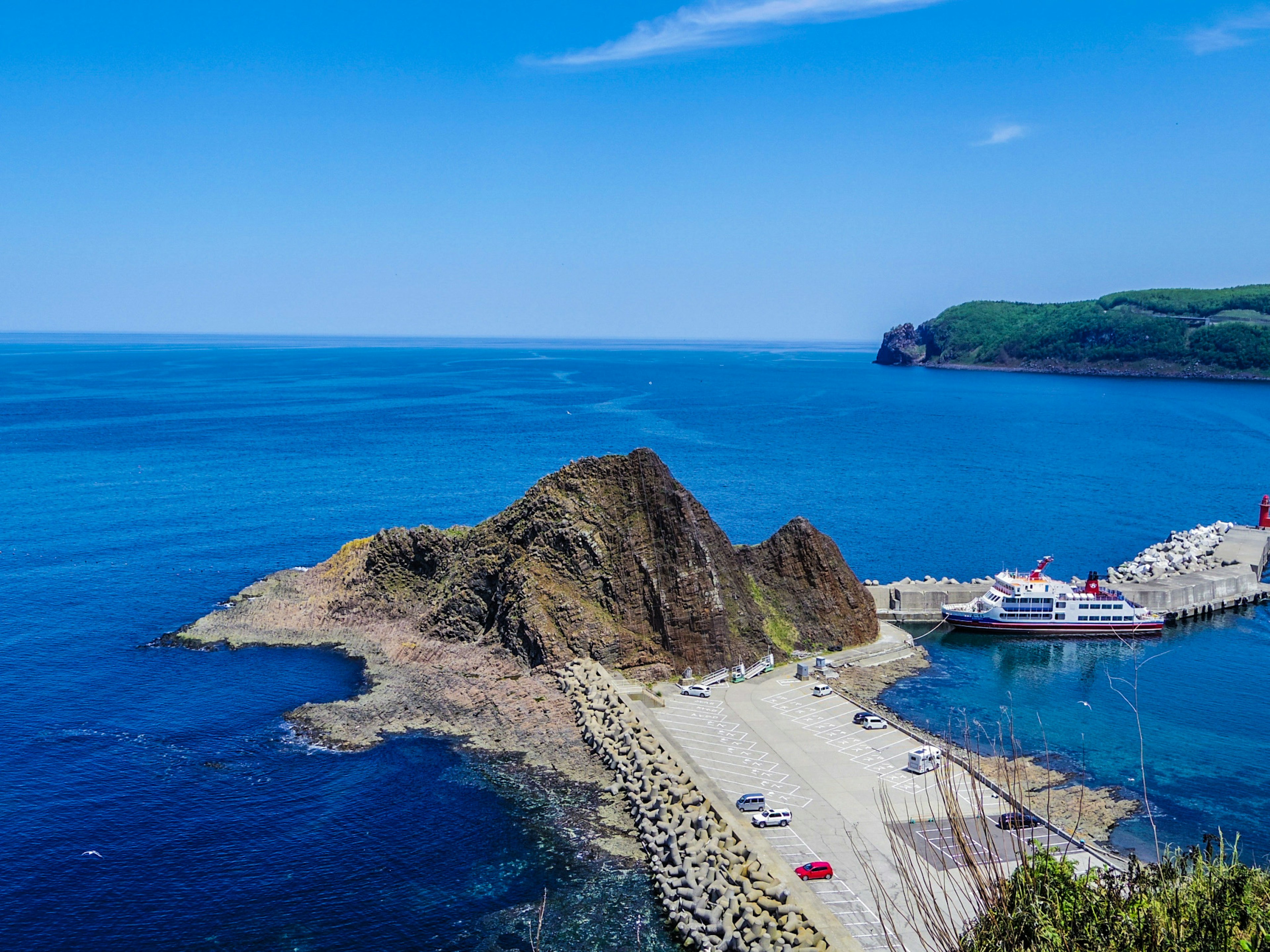 Vista escénica del mar y cielo azules con un ferry atracado en el puerto y rocas prominentes