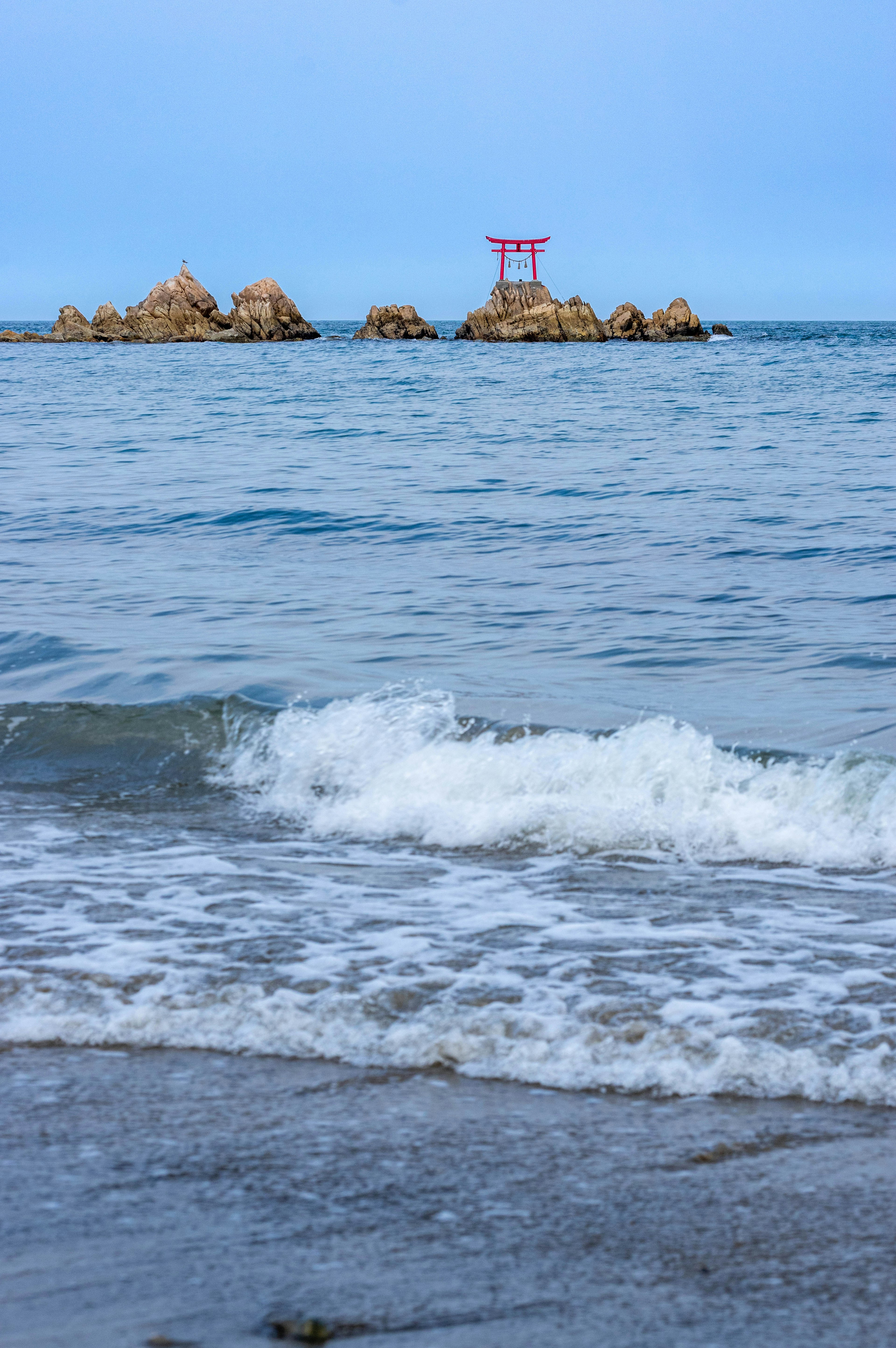 Vista panoramica di rocce costiere e un cancello torii rosso nell'oceano