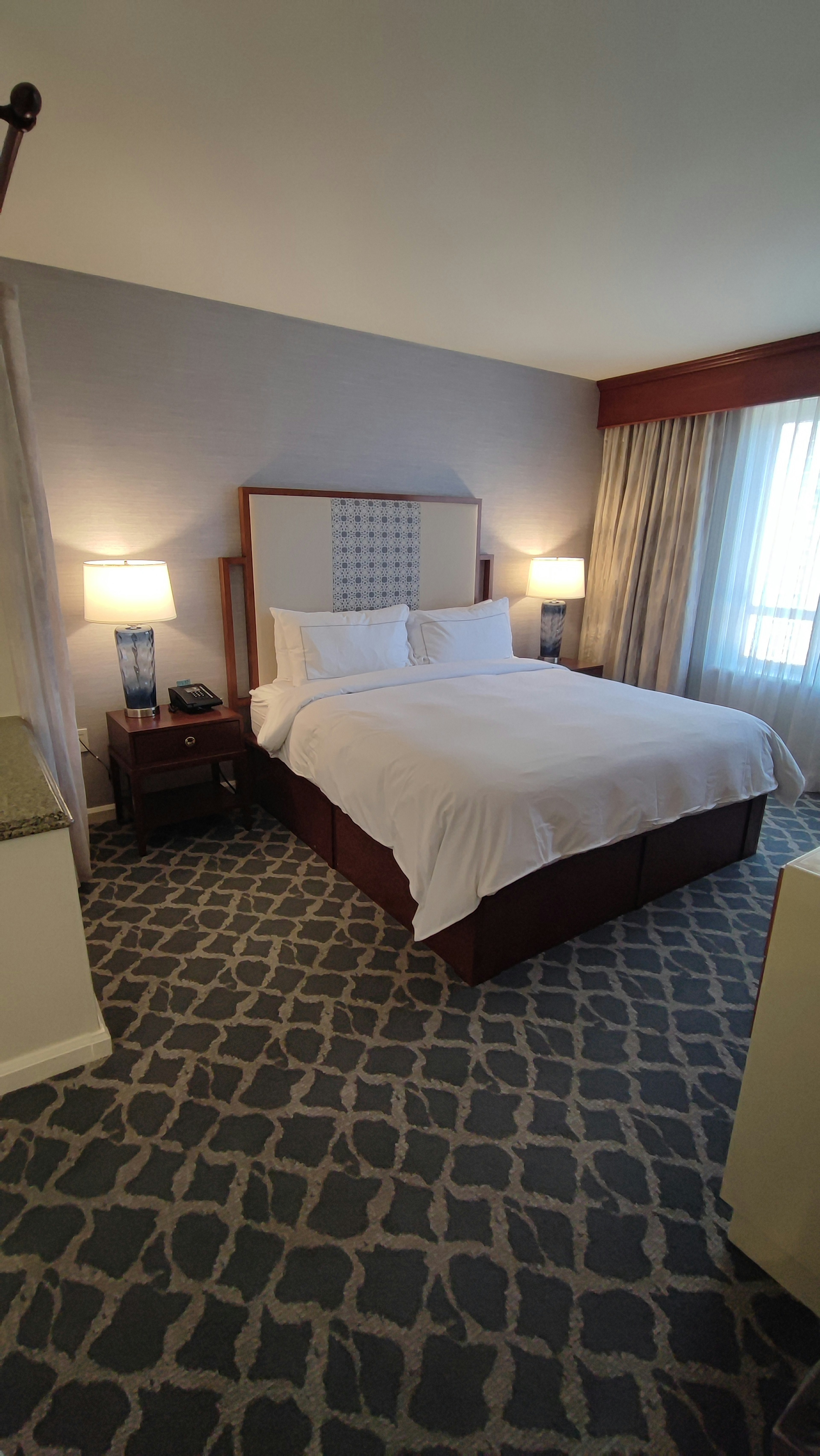 Bright hotel bedroom featuring a double bed, plush pillows, natural light from window, simple decor