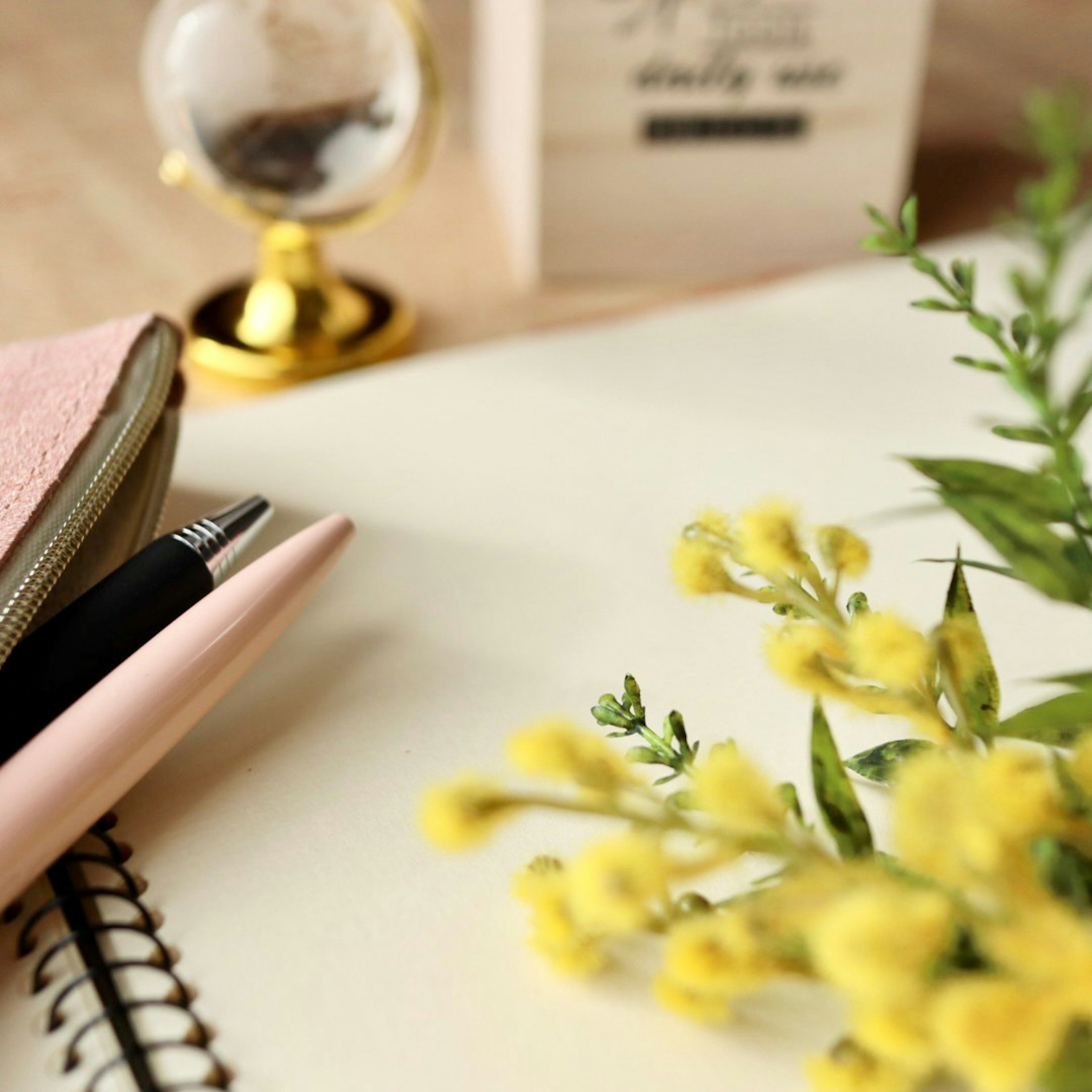 Eine Schreibtischszene mit gelben Blumen, einem rosa Stift, einem Notizbuch und einem kleinen Globus