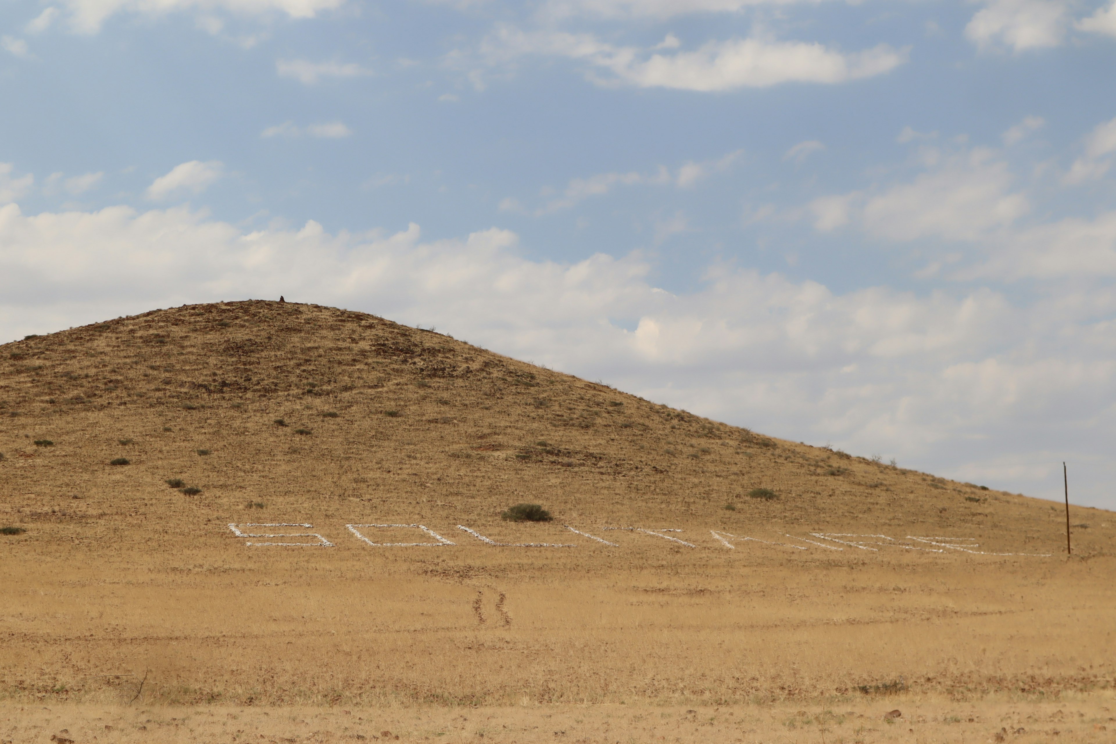 Una collina marrone con un cielo blu e nuvole bianche sullo sfondo