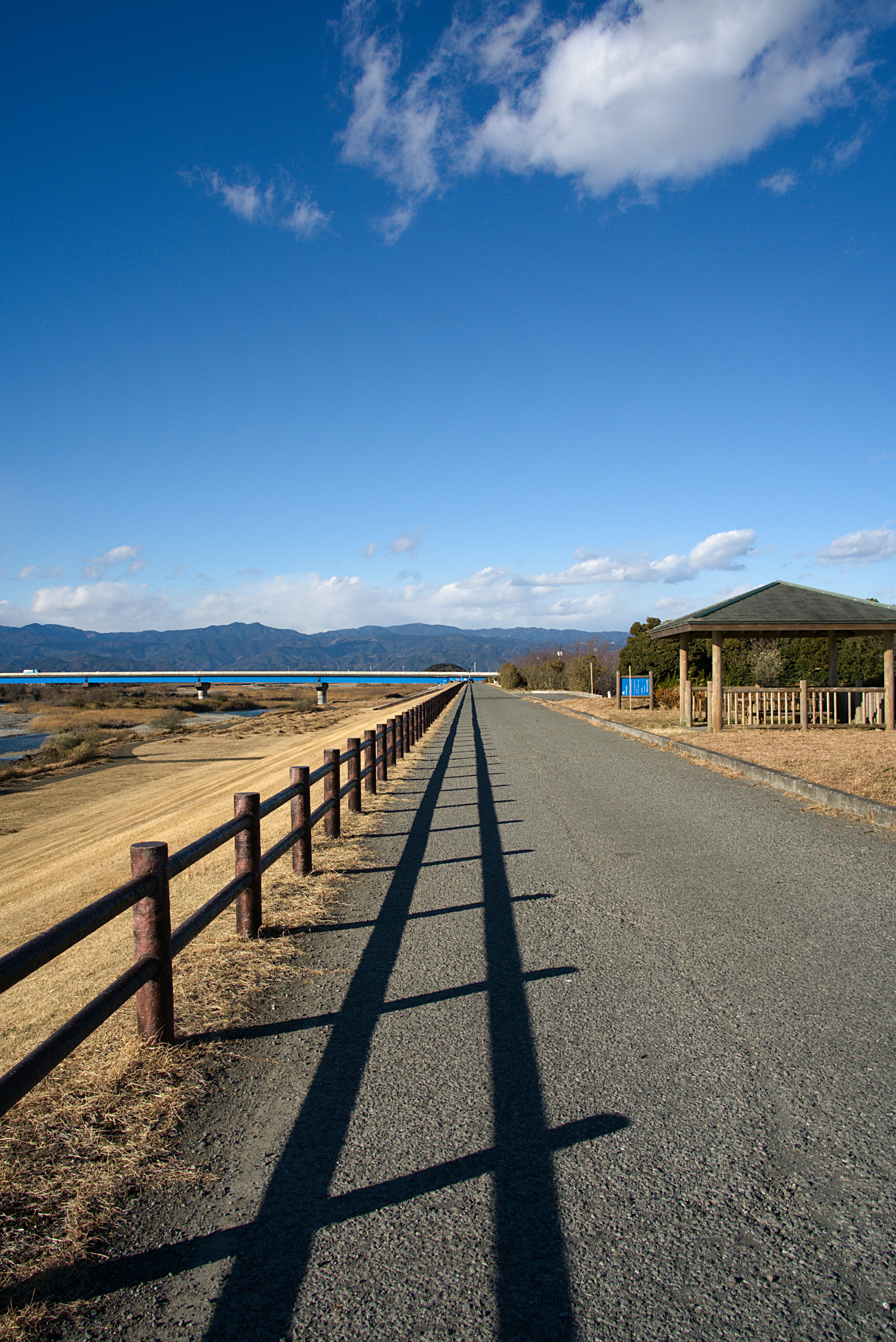 Paved road with wooden fence under blue sky and mountains