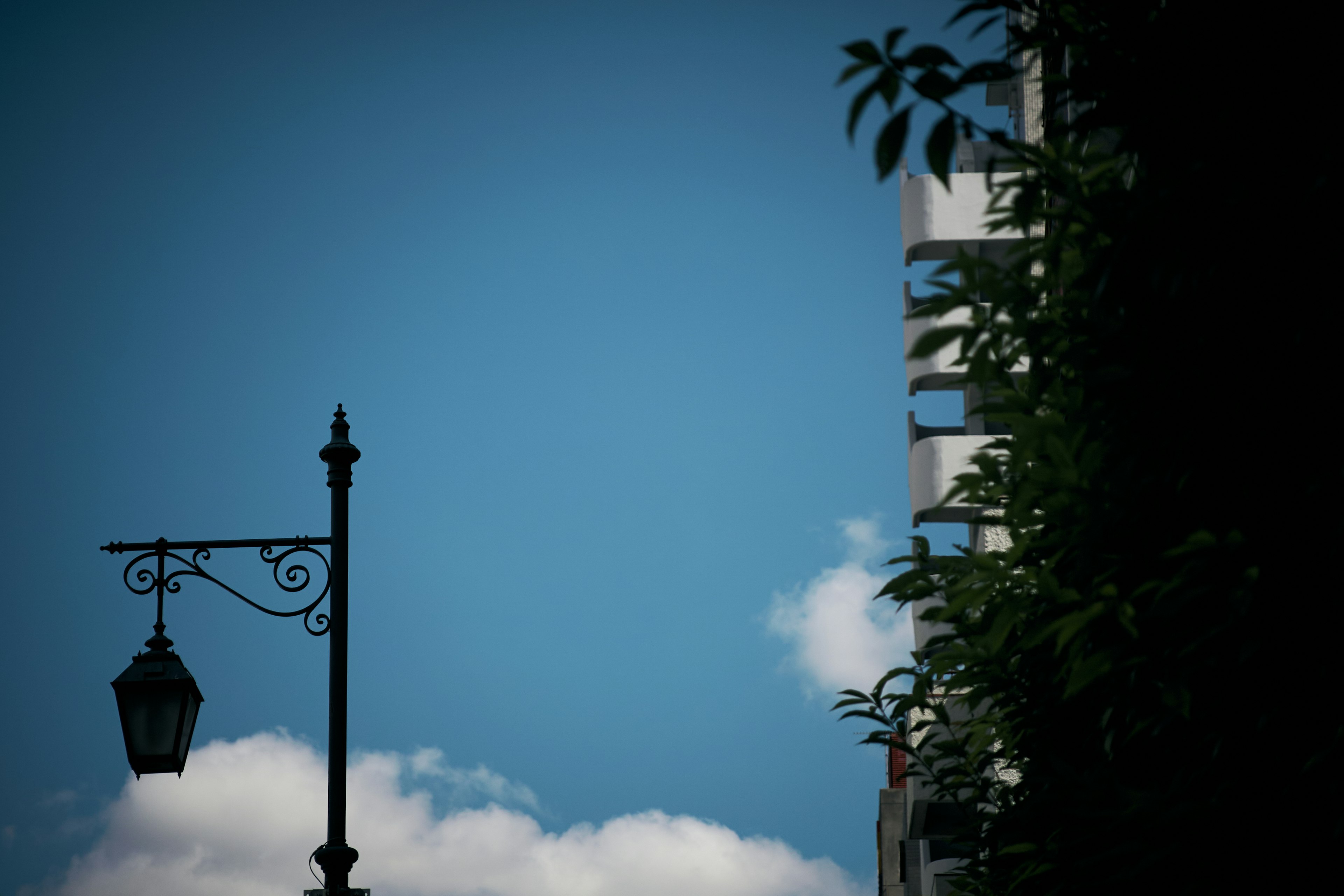 Silhouette of a street lamp against a blue sky with white clouds