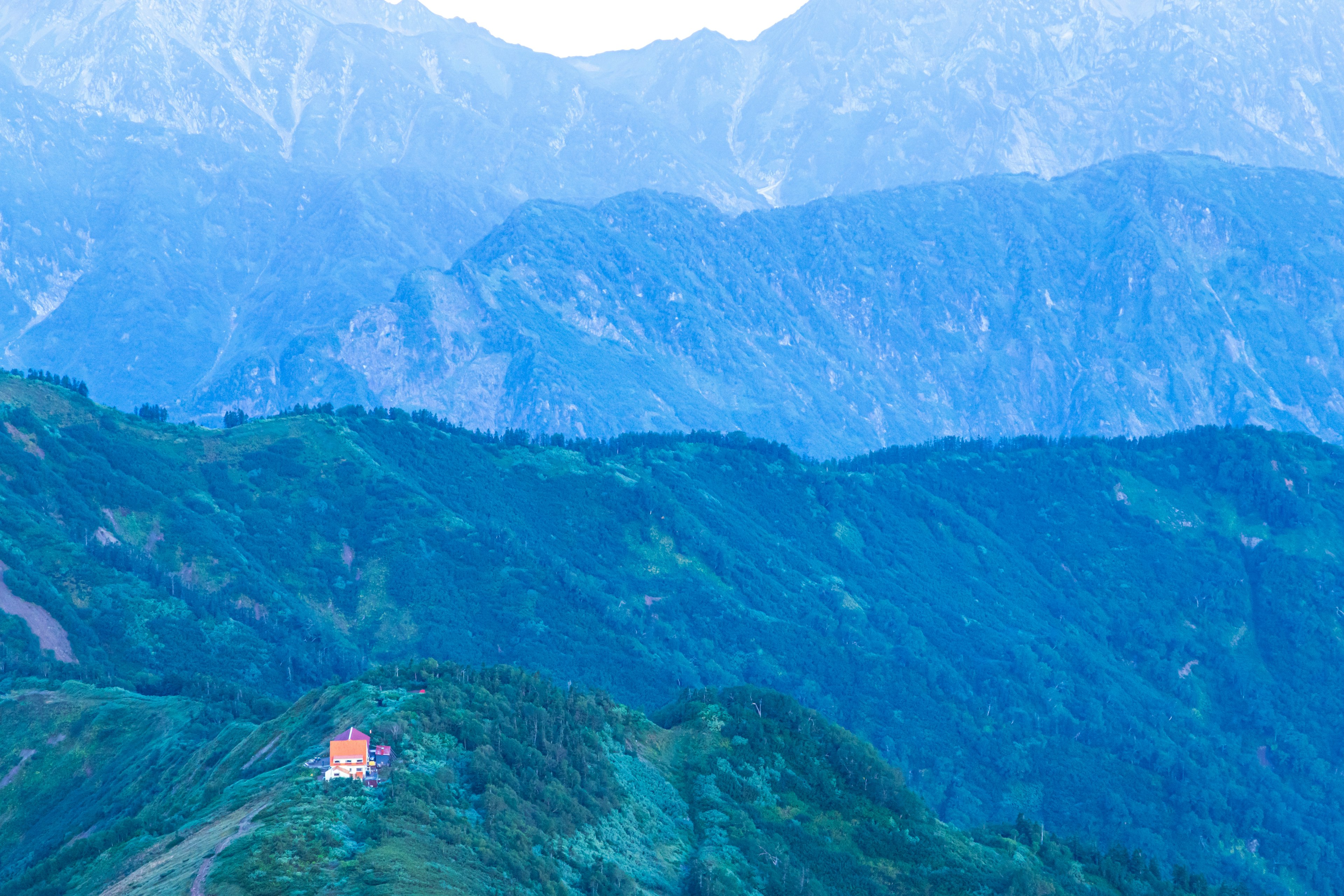 Un paysage de montagnes bleues avec un petit bâtiment rouge au premier plan