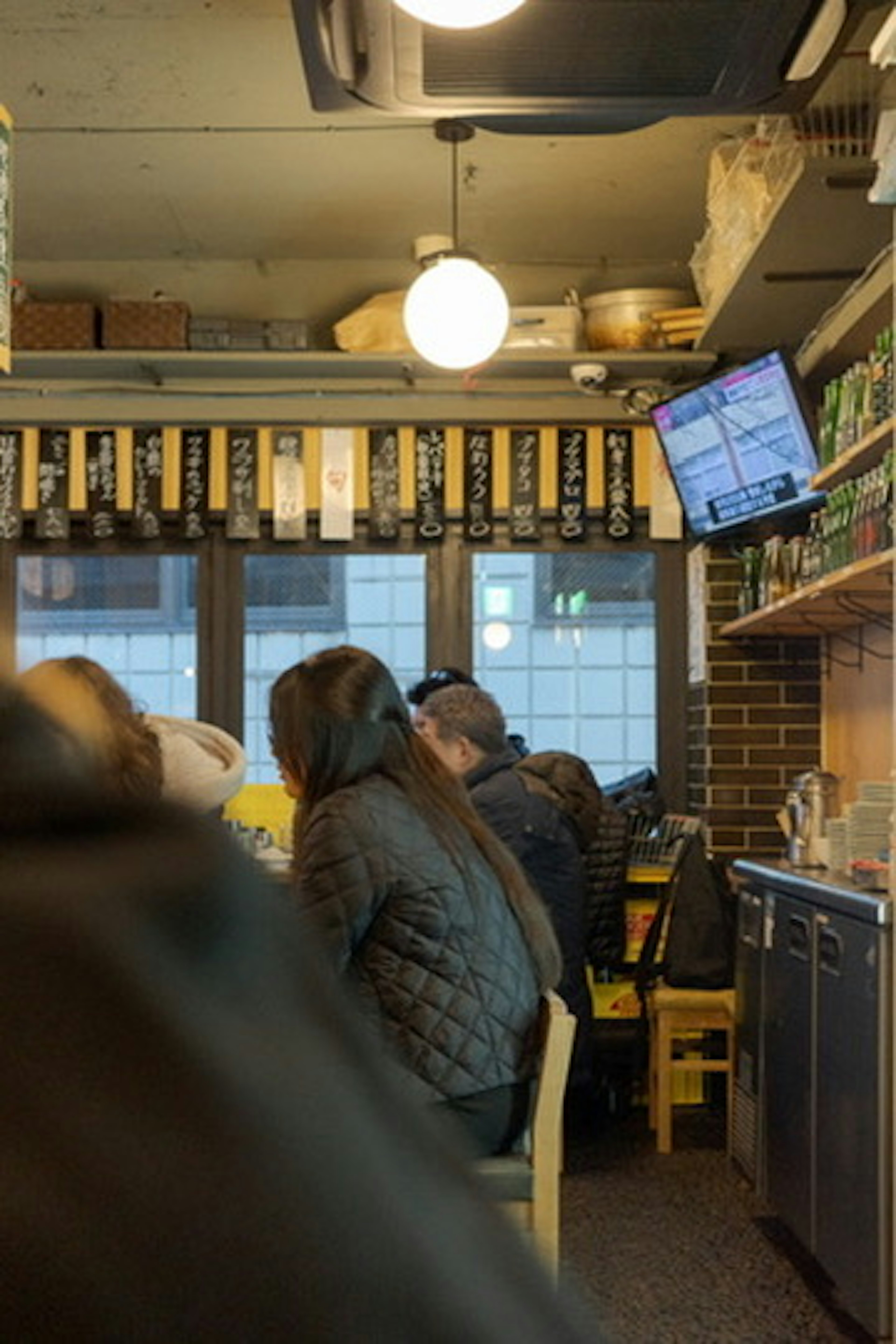 Interior of an izakaya with people seated Lighting and a television present