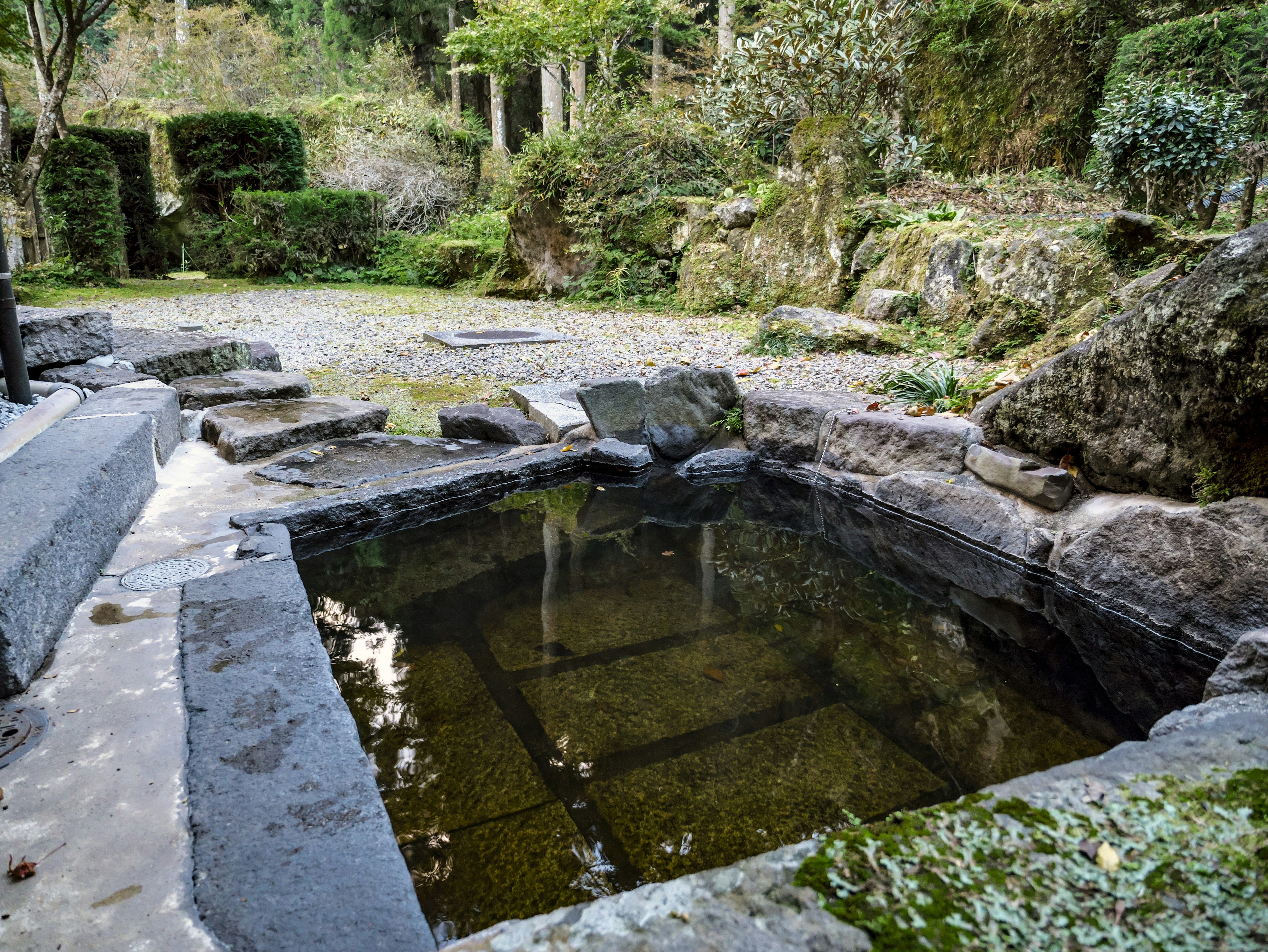 Jardín sereno con una piscina termal de piedra rodeada de paisajes naturales