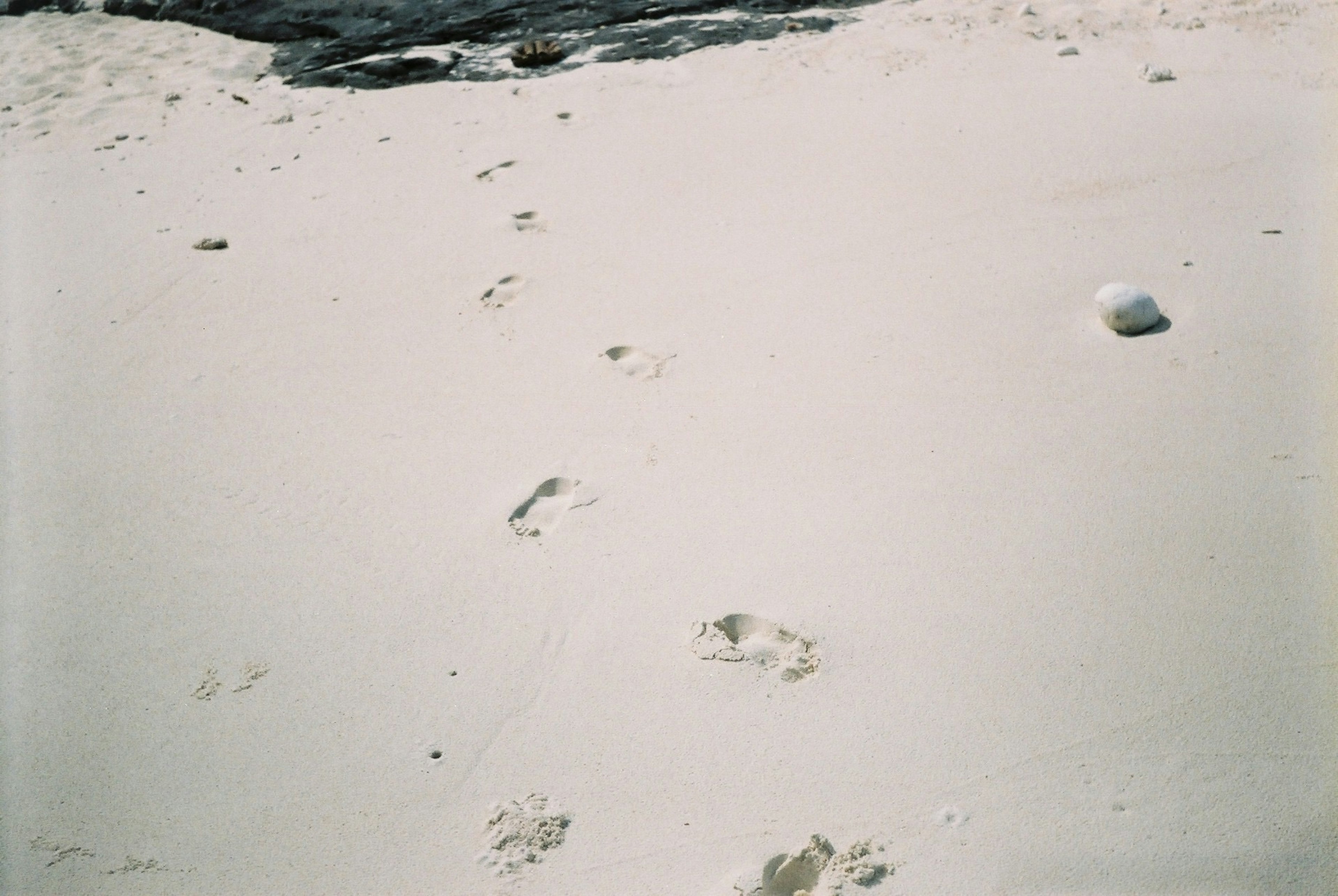 Footprints on a white sandy beach with rocks