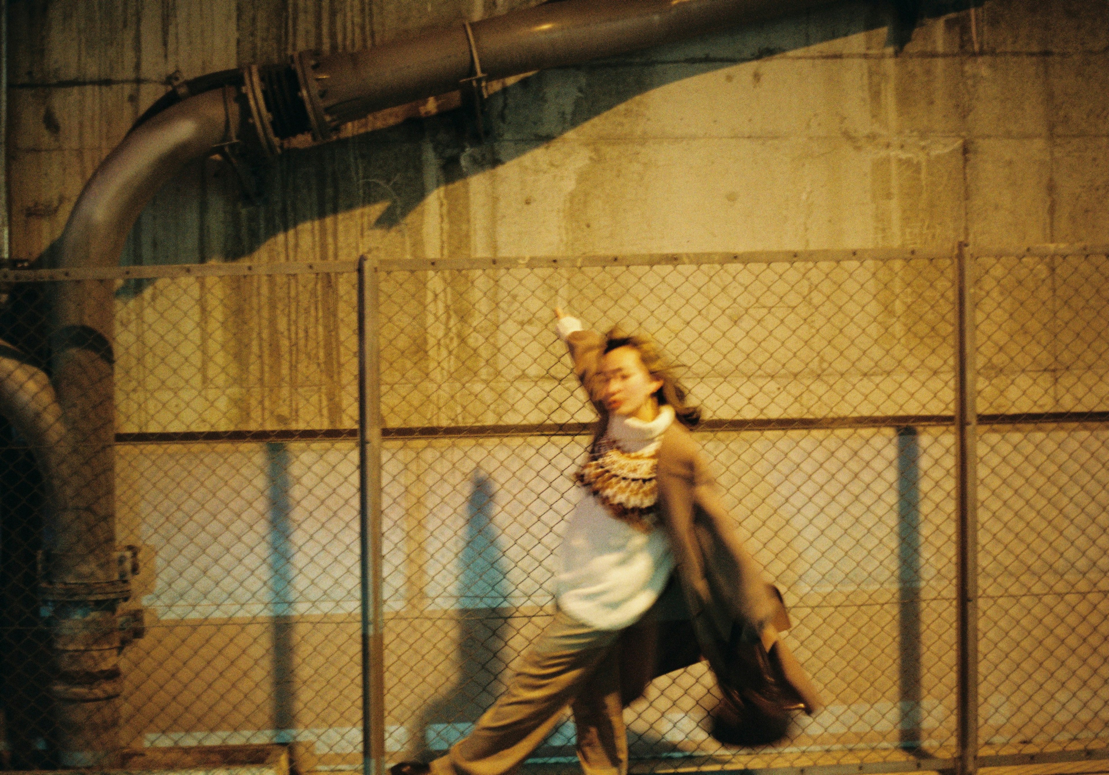 Une femme prenant une pose dans un cadre urbain avec des tuyaux en métal et une clôture en arrière-plan