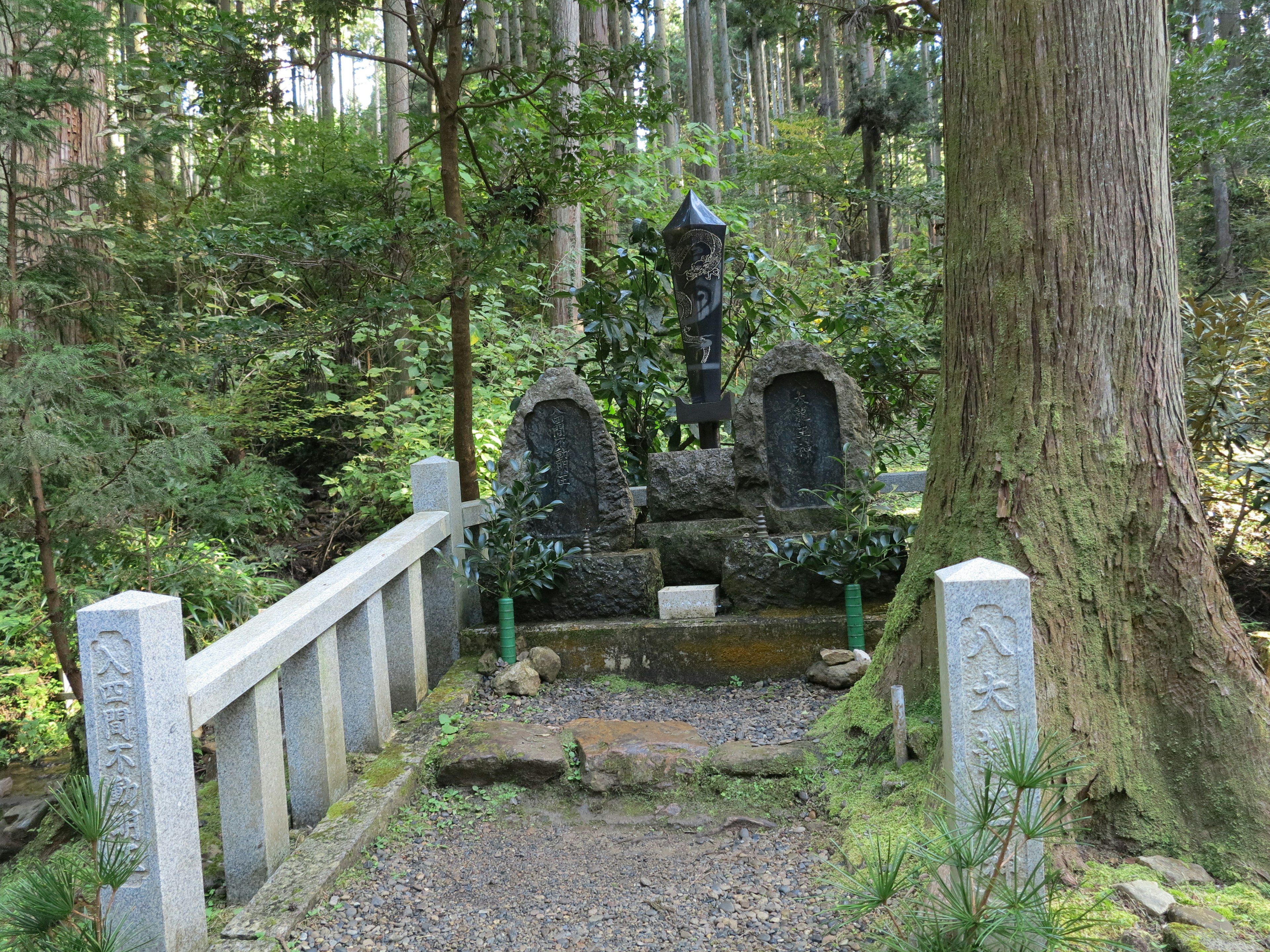 Pemandangan pemakaman tenang di hutan dengan monumen batu tua dan patung biru