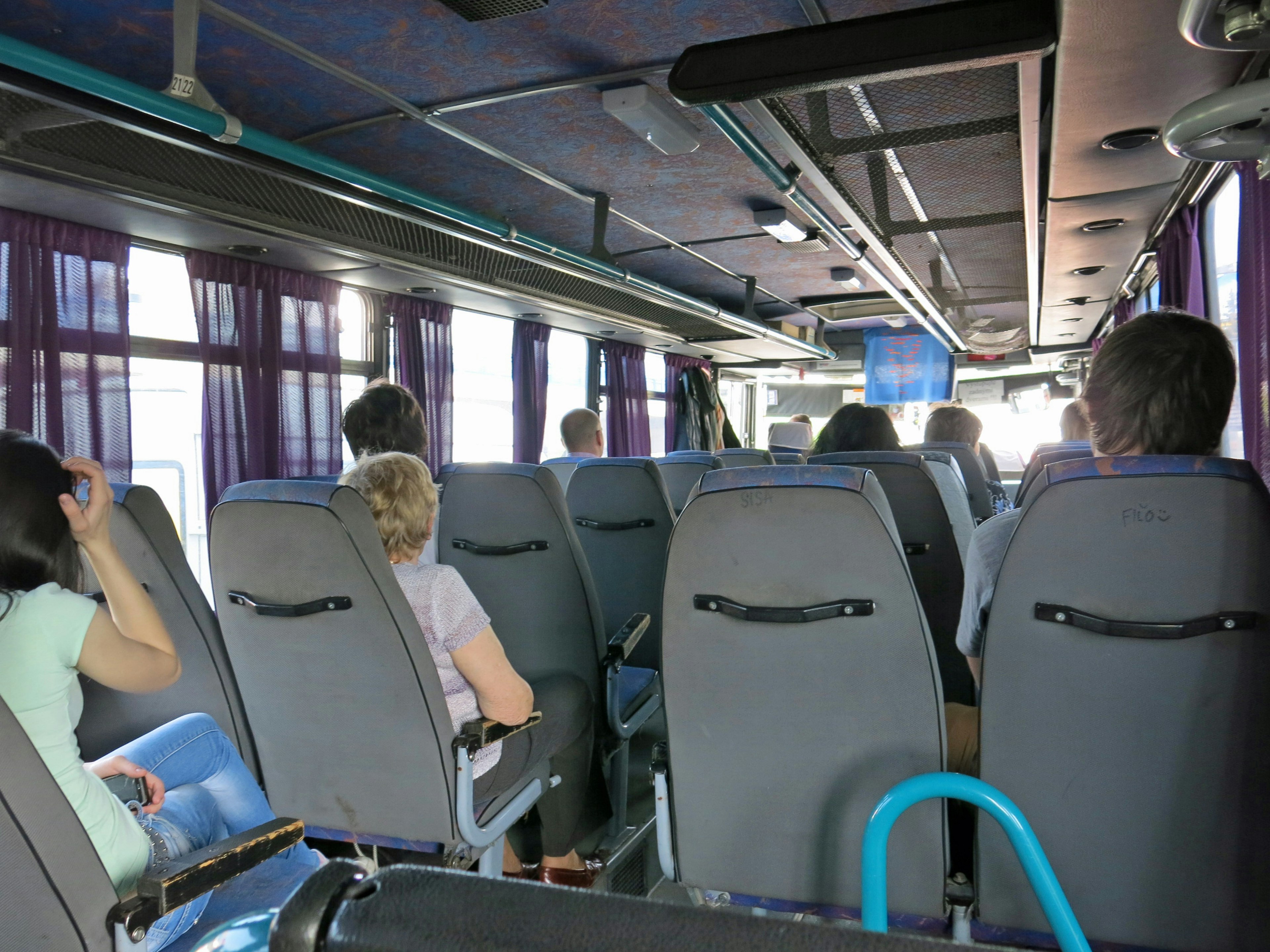 Innenansicht eines Busses mit sitzenden Passagieren und lila Vorhängen