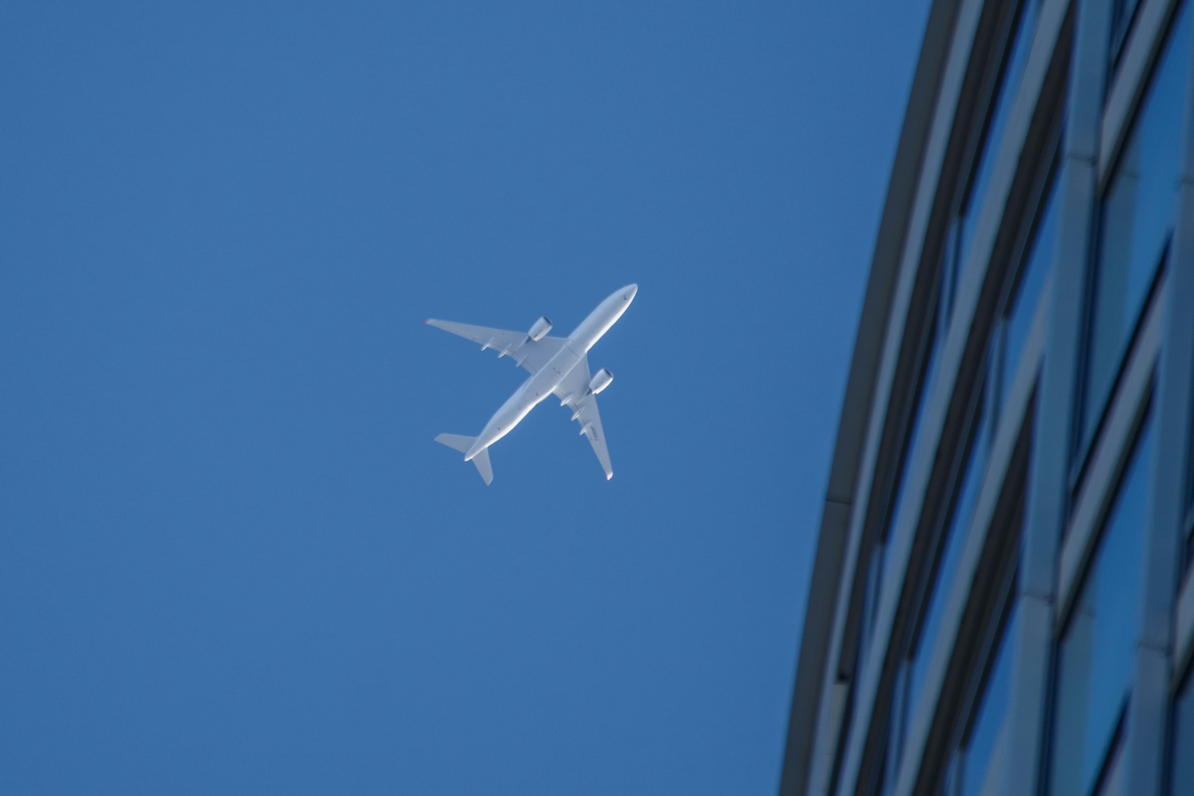 Airplane flying in blue sky alongside building