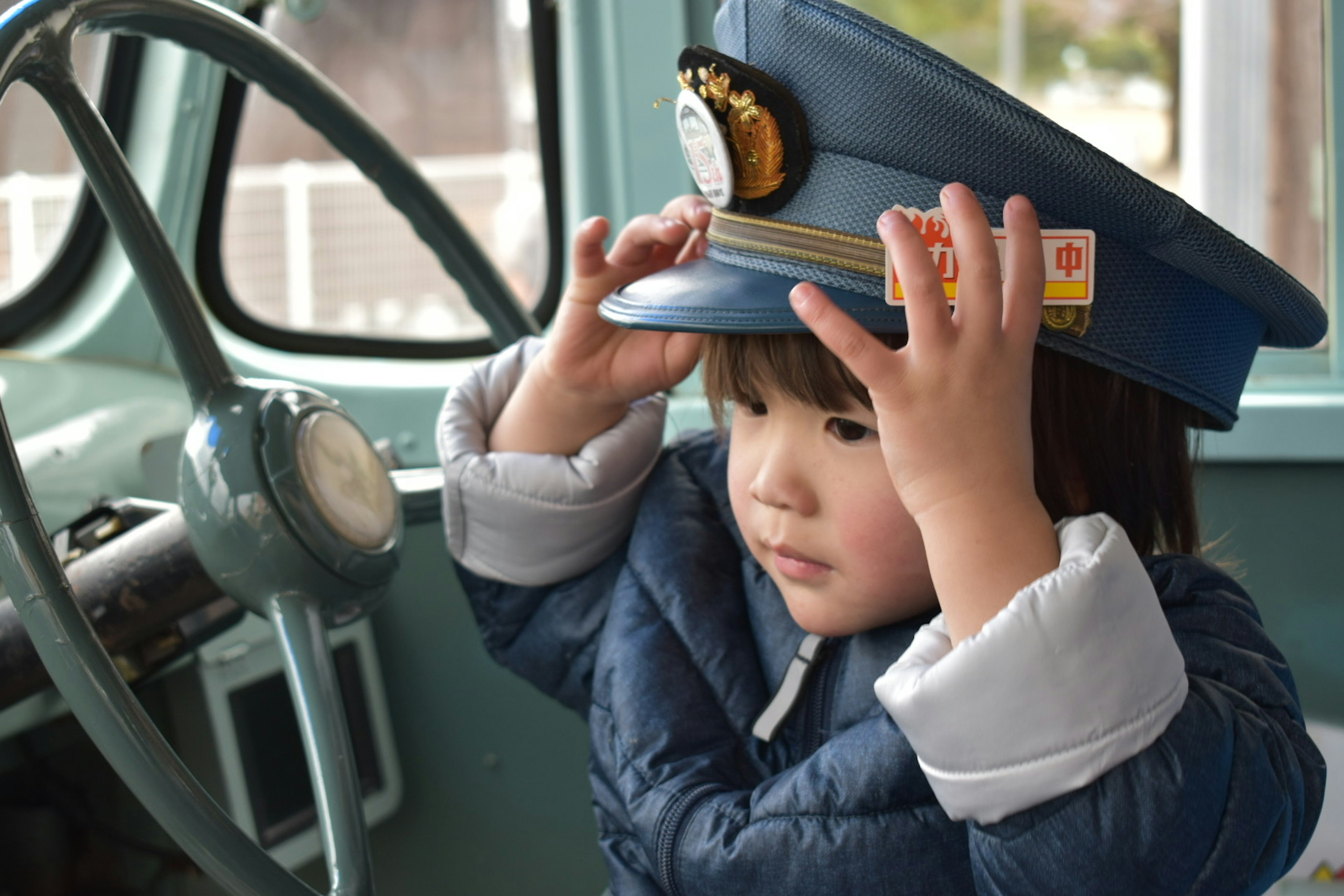 Child wearing a blue police hat sitting in a vintage vehicle's driver's seat