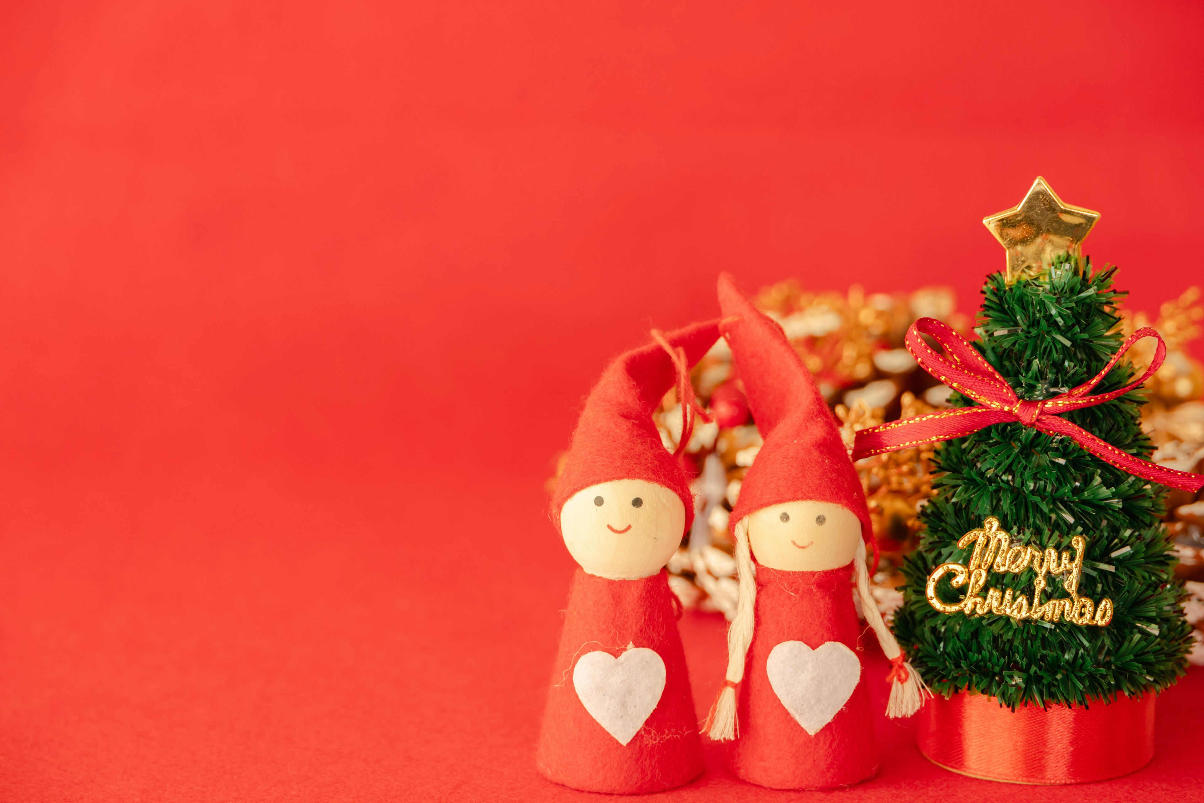 Two Christmas figures in red outfits with hearts beside a small Christmas tree