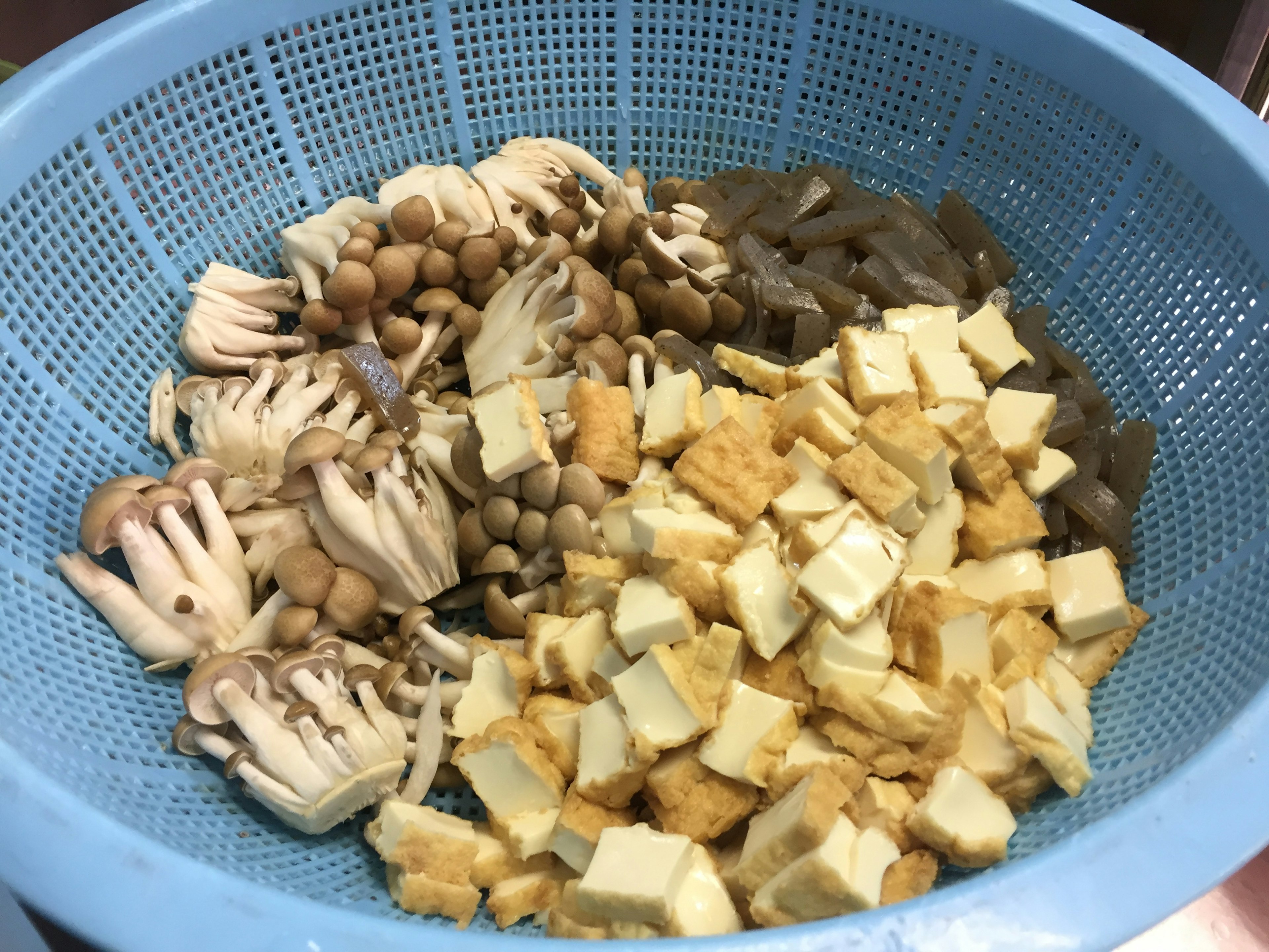 A blue colander filled with various mushrooms and tofu cubes