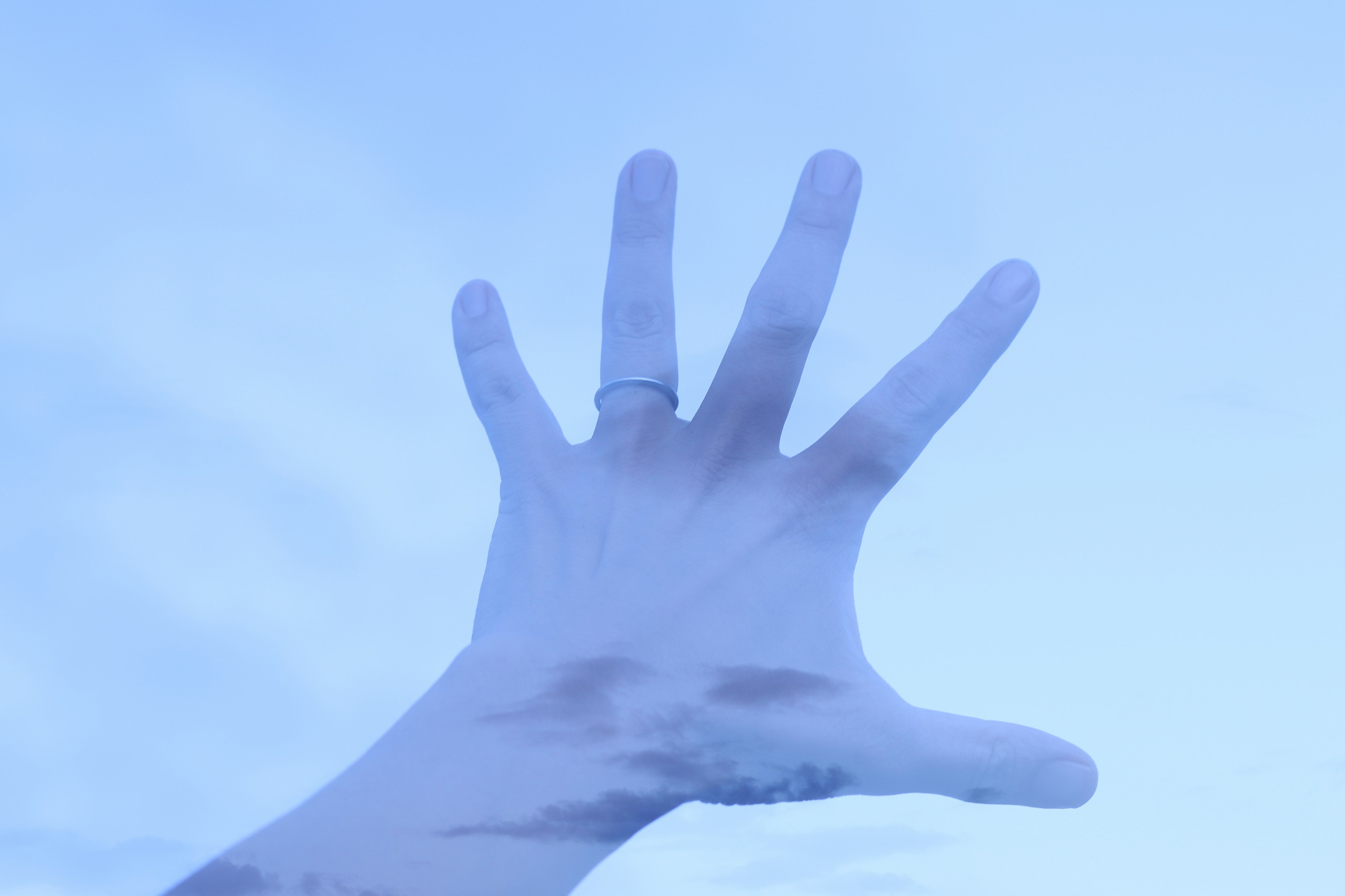 A hand reaching upward against a blue sky background