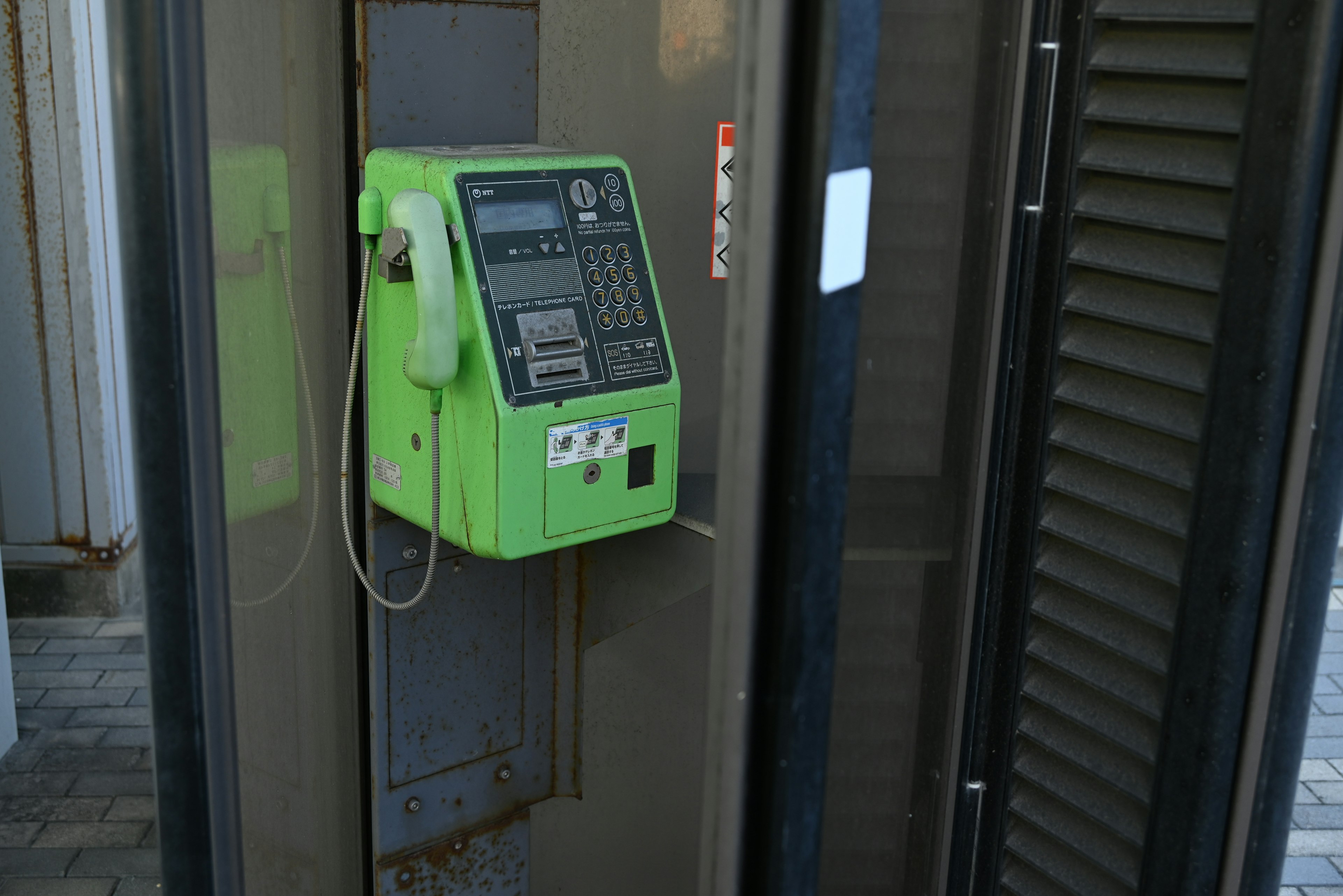 Imagen de un teléfono público verde dentro de una cabina telefónica