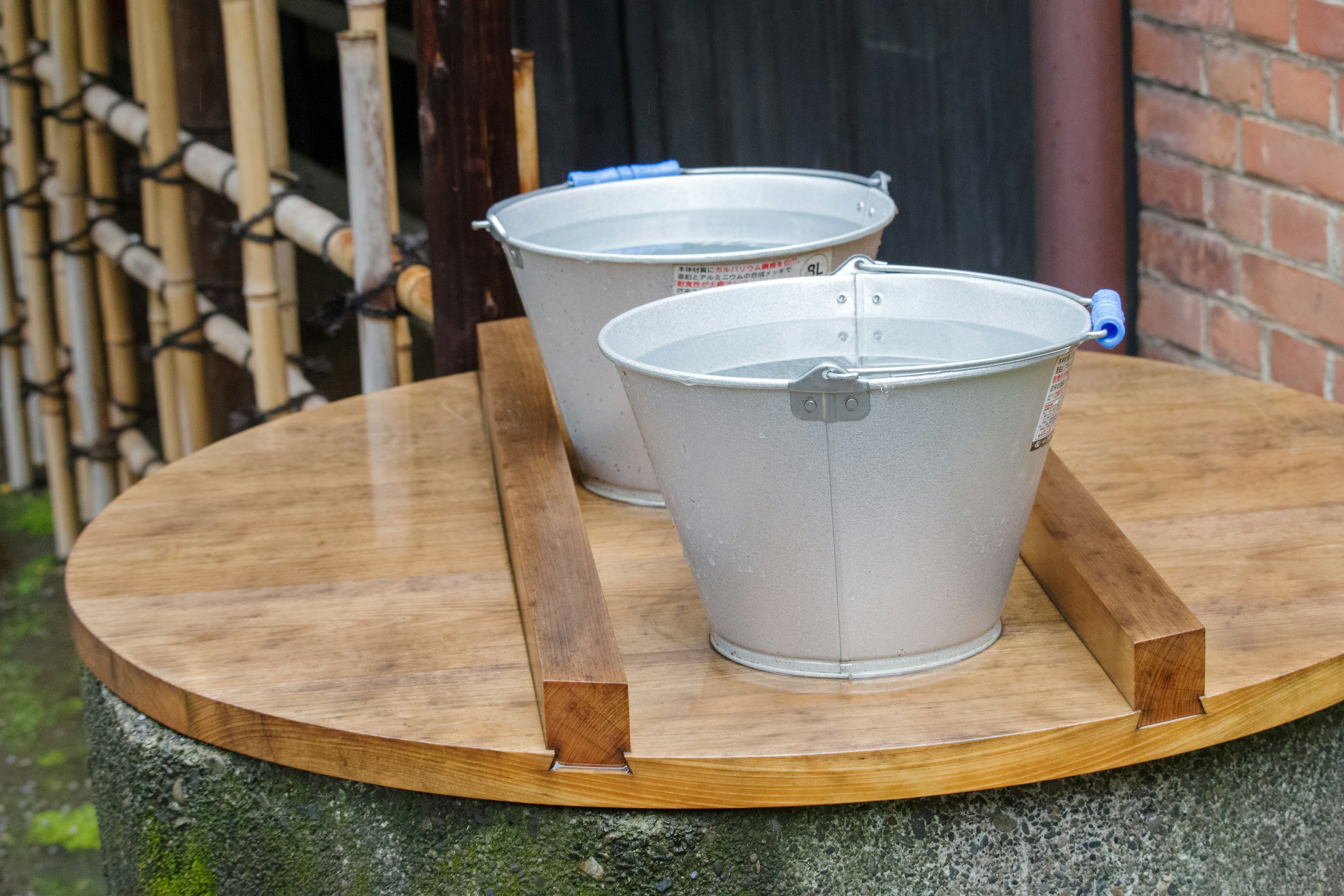 Two metal buckets on a wooden platform with a bamboo background