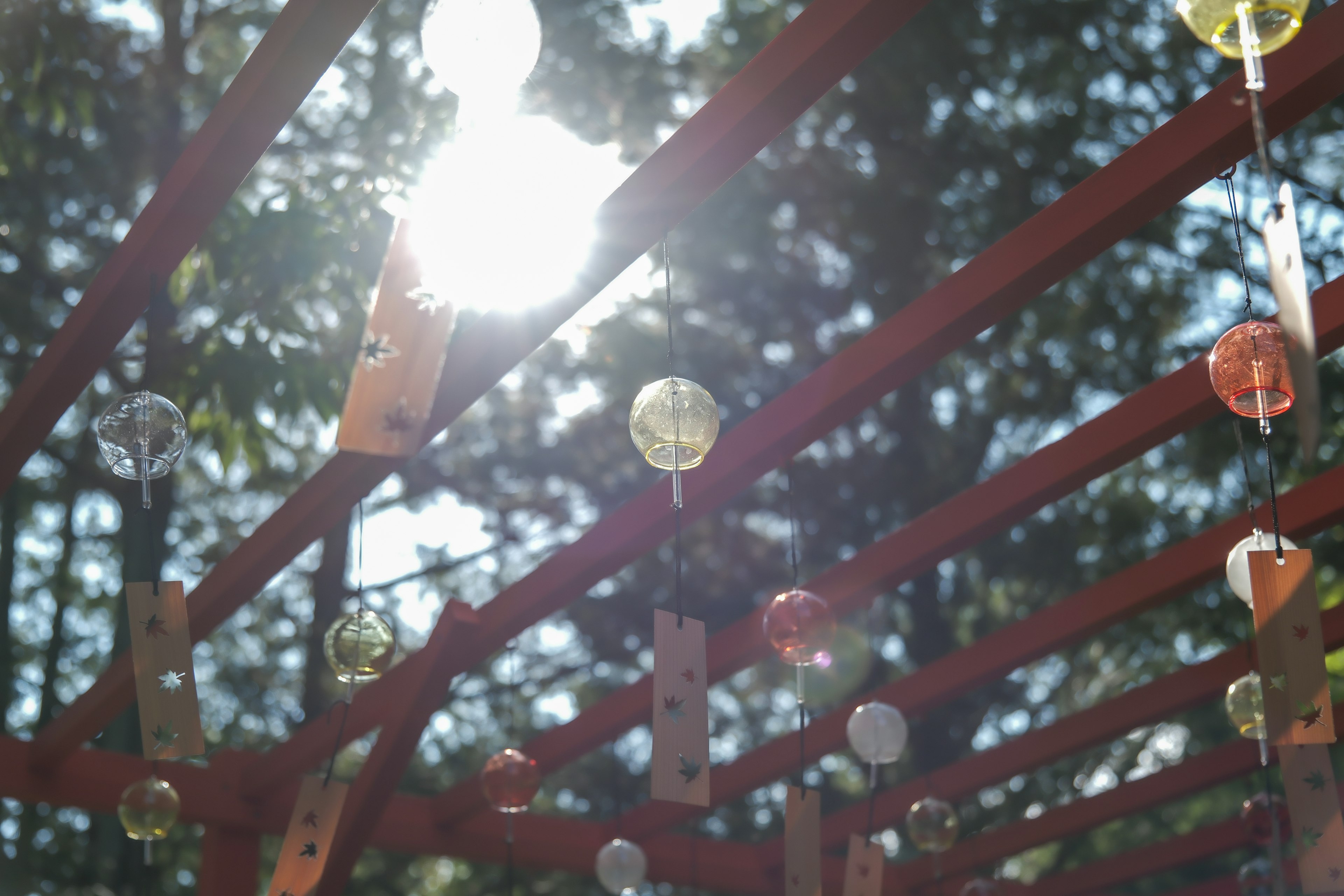 Bunte Glaskugeln hängen von einer roten Holzstruktur mit Sonnenlicht