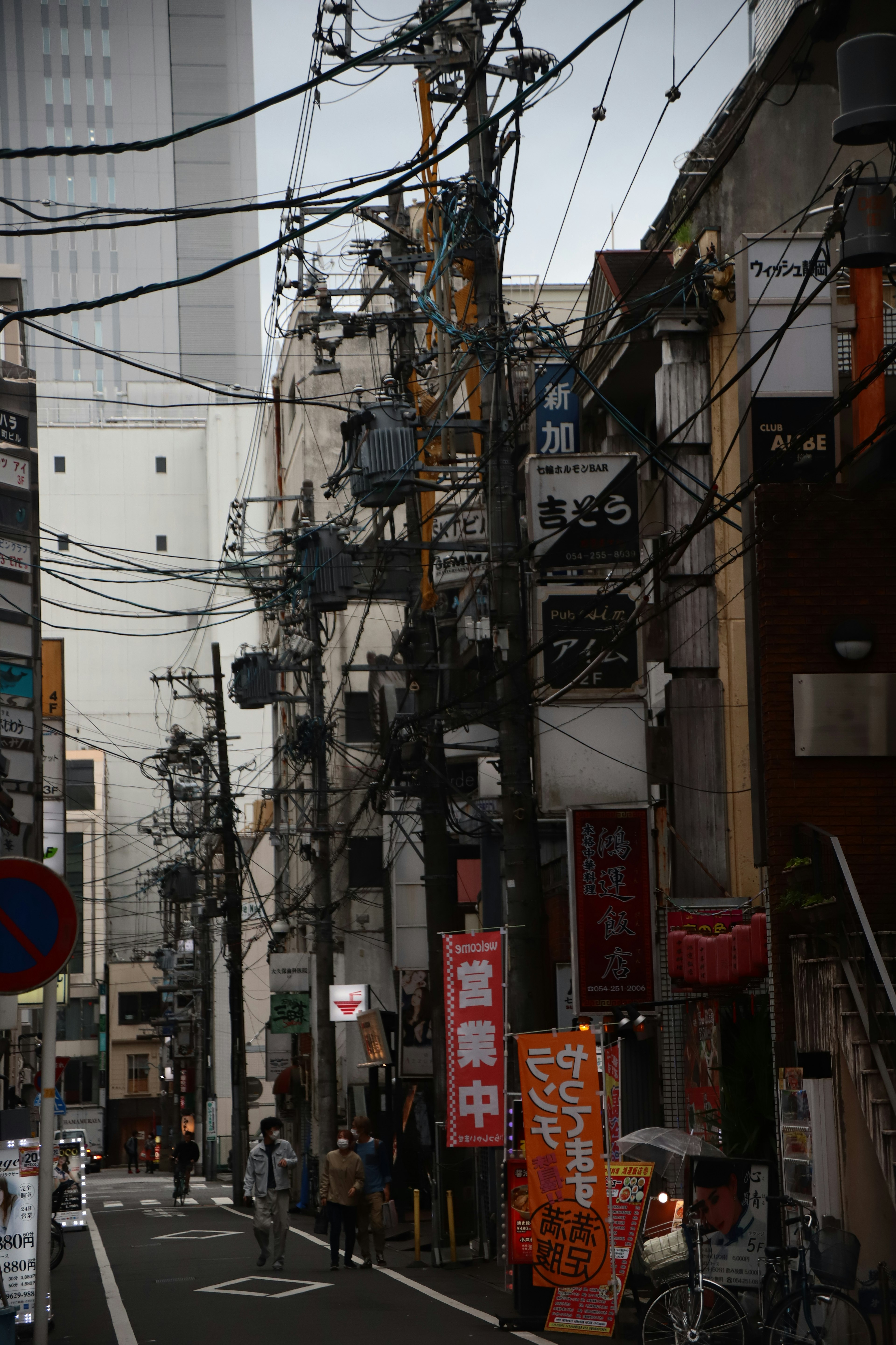 ถนนแคบในโตเกียวที่มีสายไฟข้ามและผู้คนเดิน