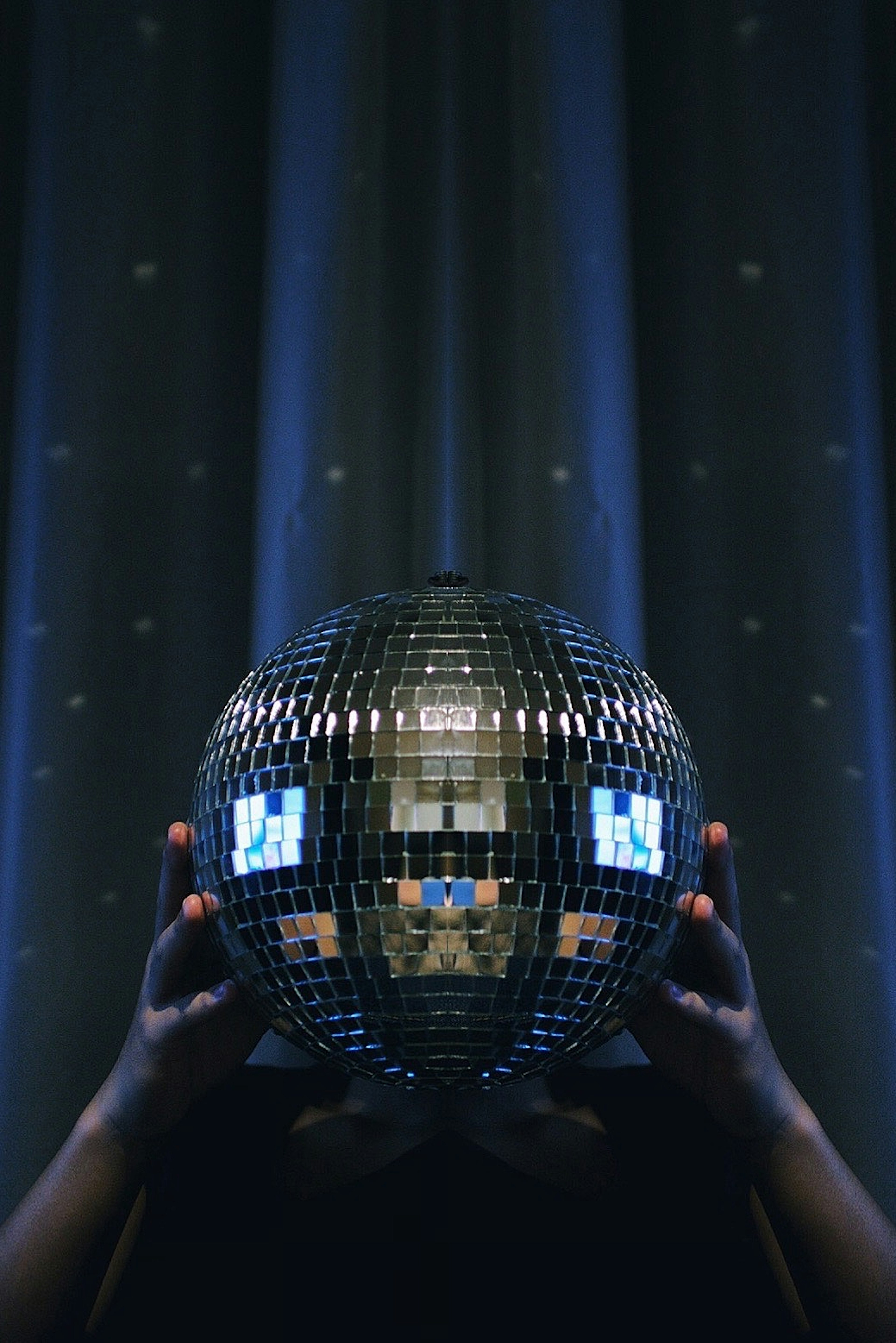 A person holding a reflective disco ball with a dark background