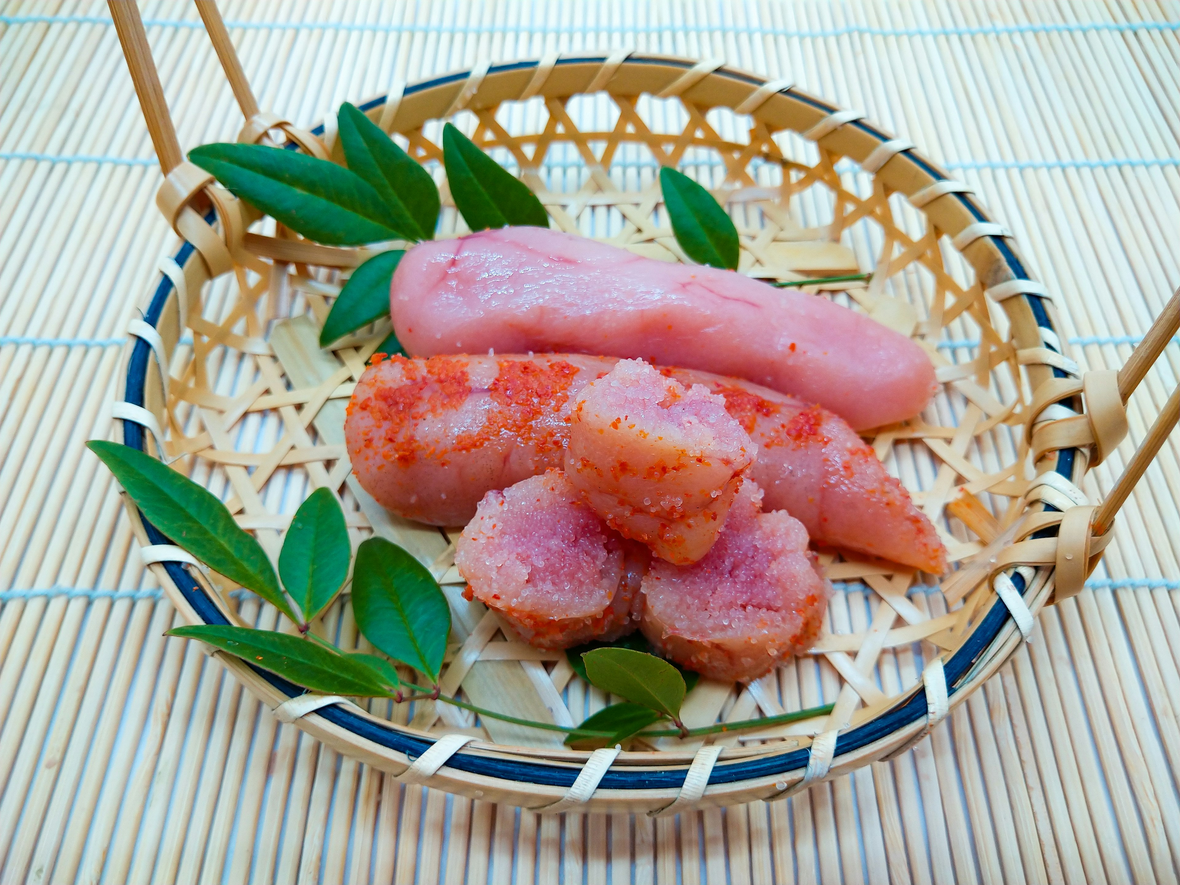 Huevas de pescado rosa dispuestas en una canasta de bambú con hojas verdes