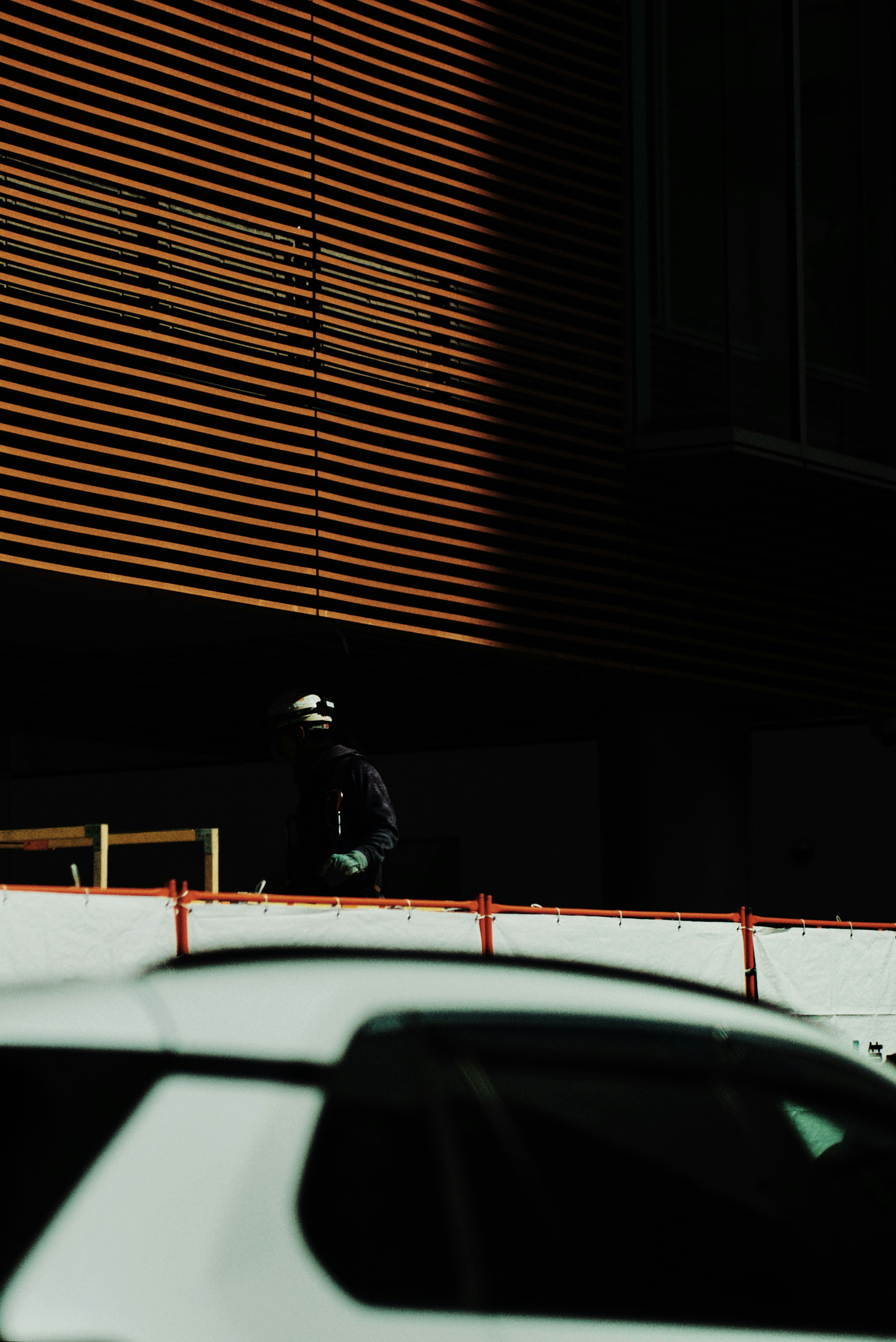 Worker standing in shadow next to white car and building wall