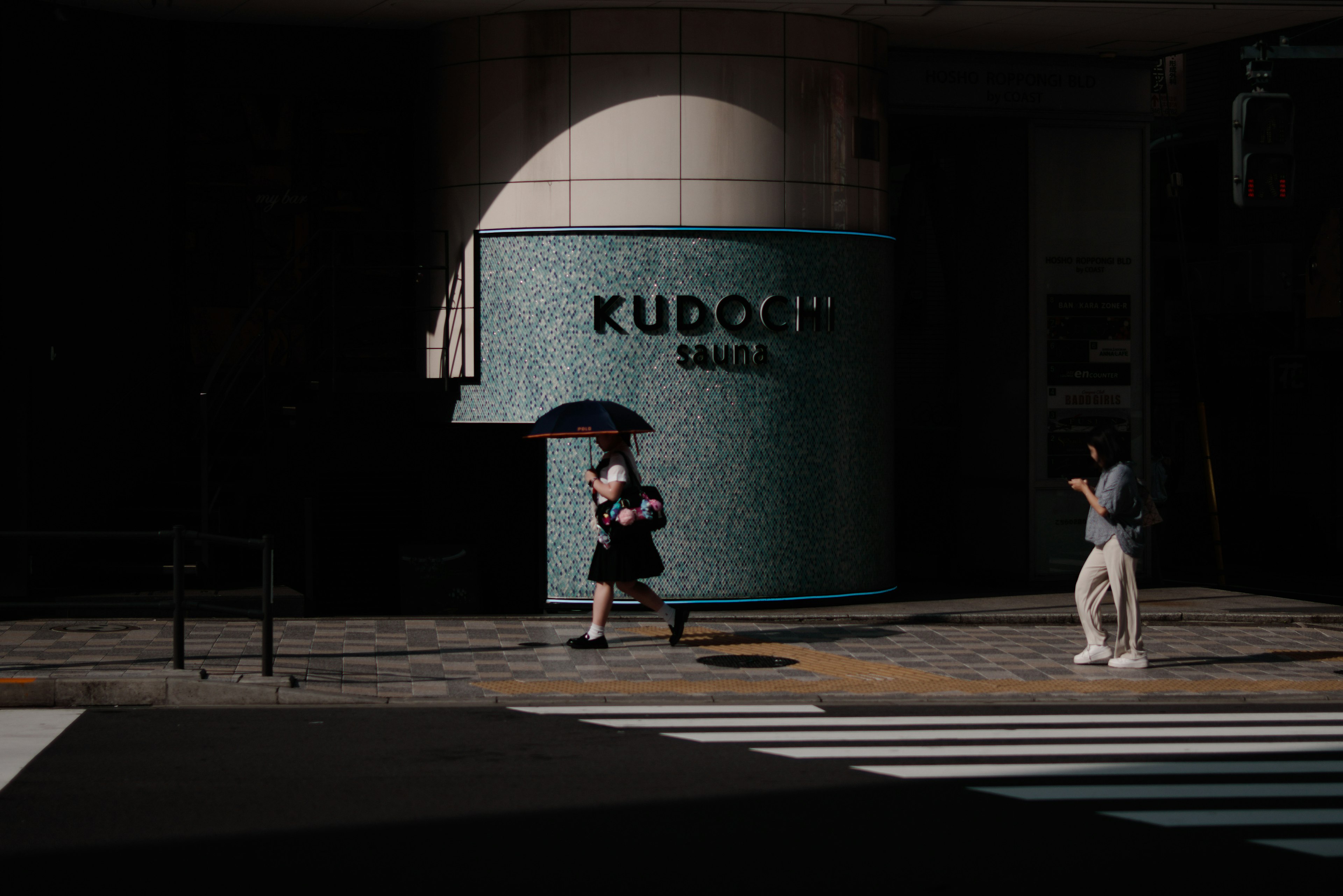 一位女性在昏暗的街道上走，手持雨伞，背景是KUDOKU标志