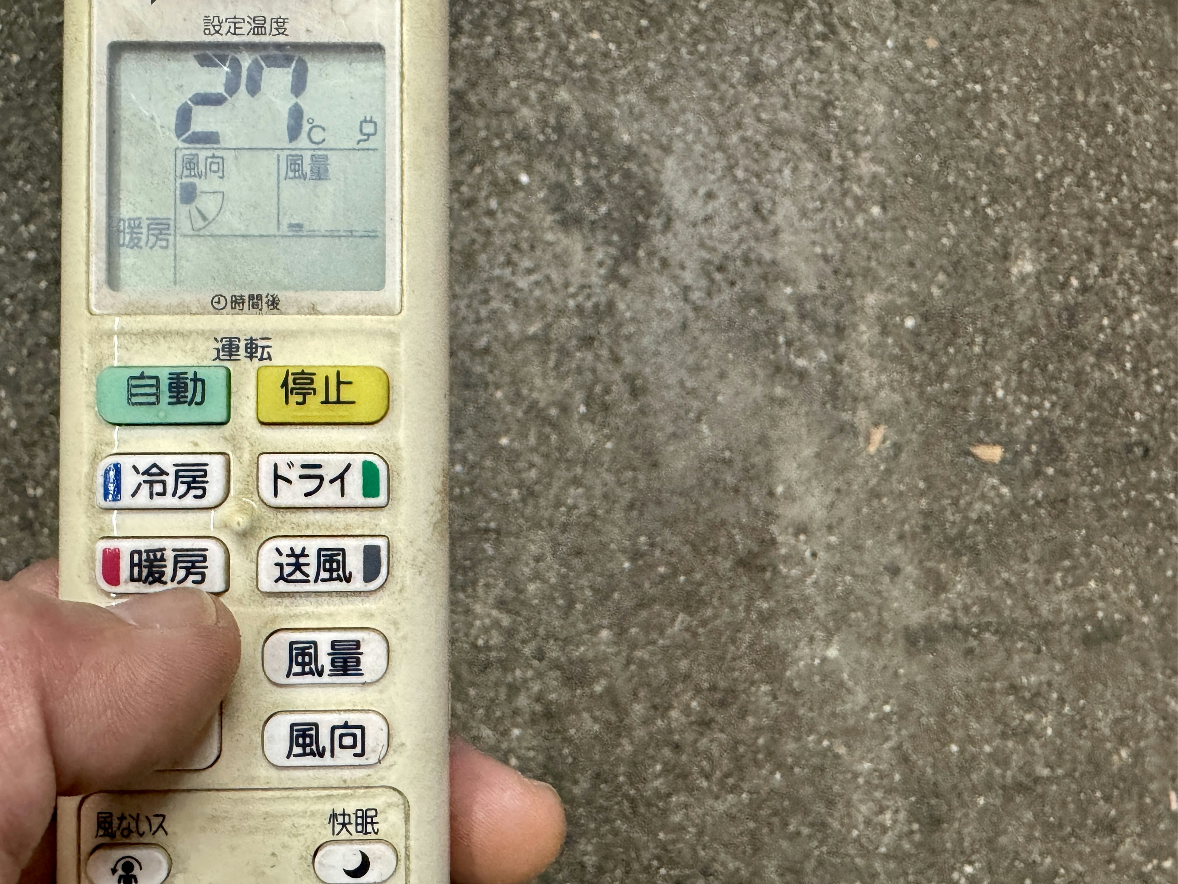 Hand holding a remote control with a concrete surface in the background