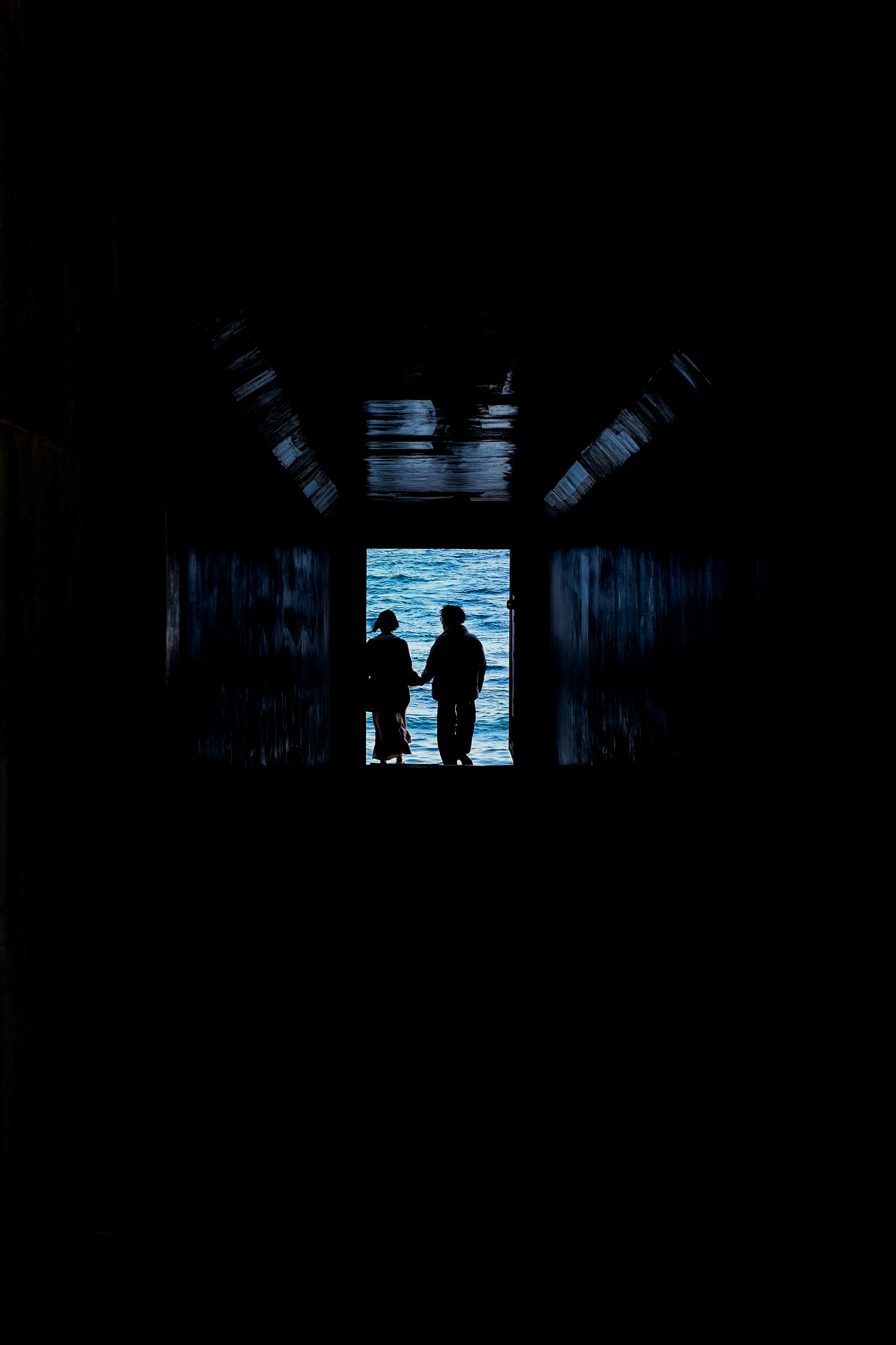 Silhouette of two people holding hands in a dark tunnel with ocean view