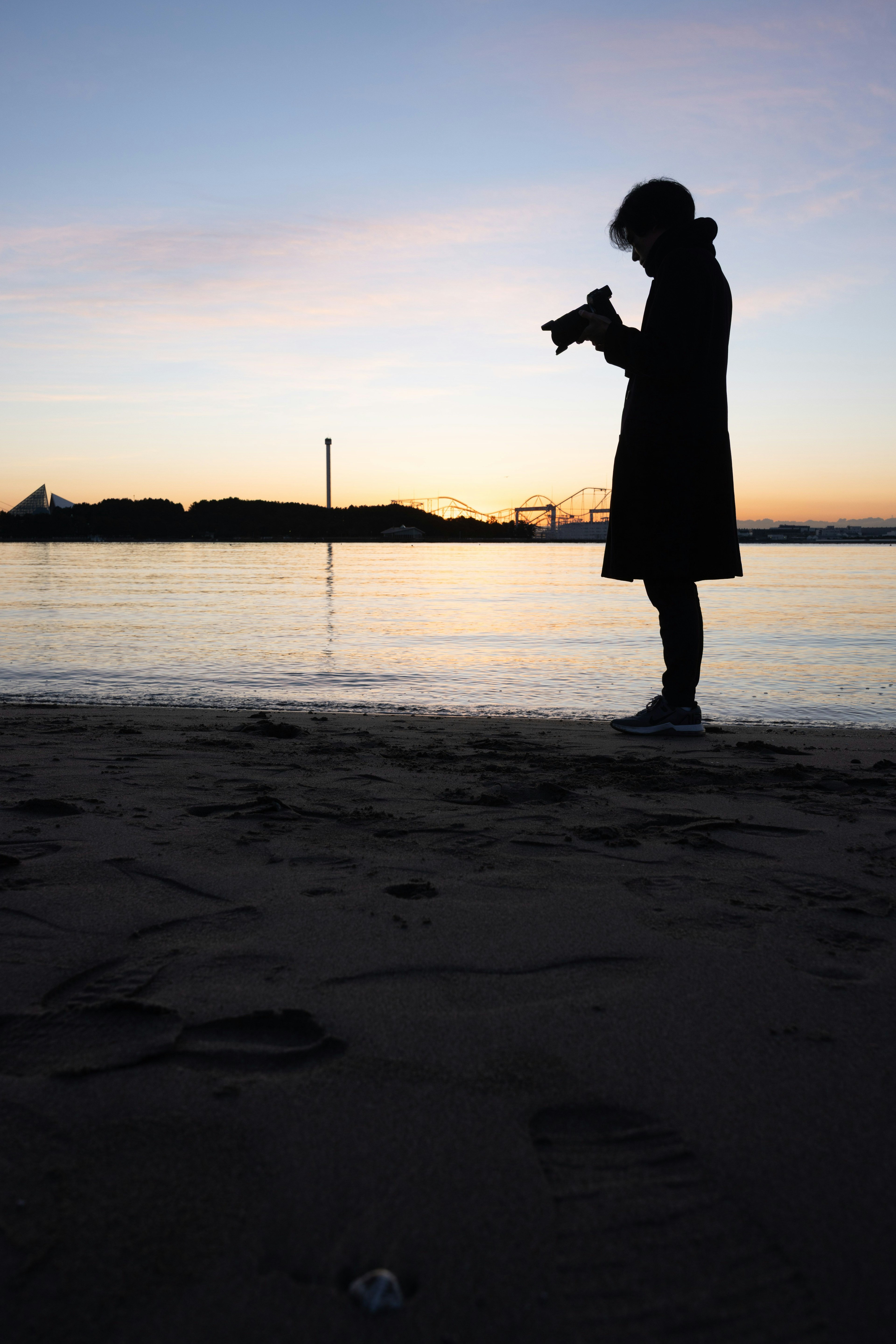 夕暮れ時の海岸でシルエットの人物がカメラを持っている