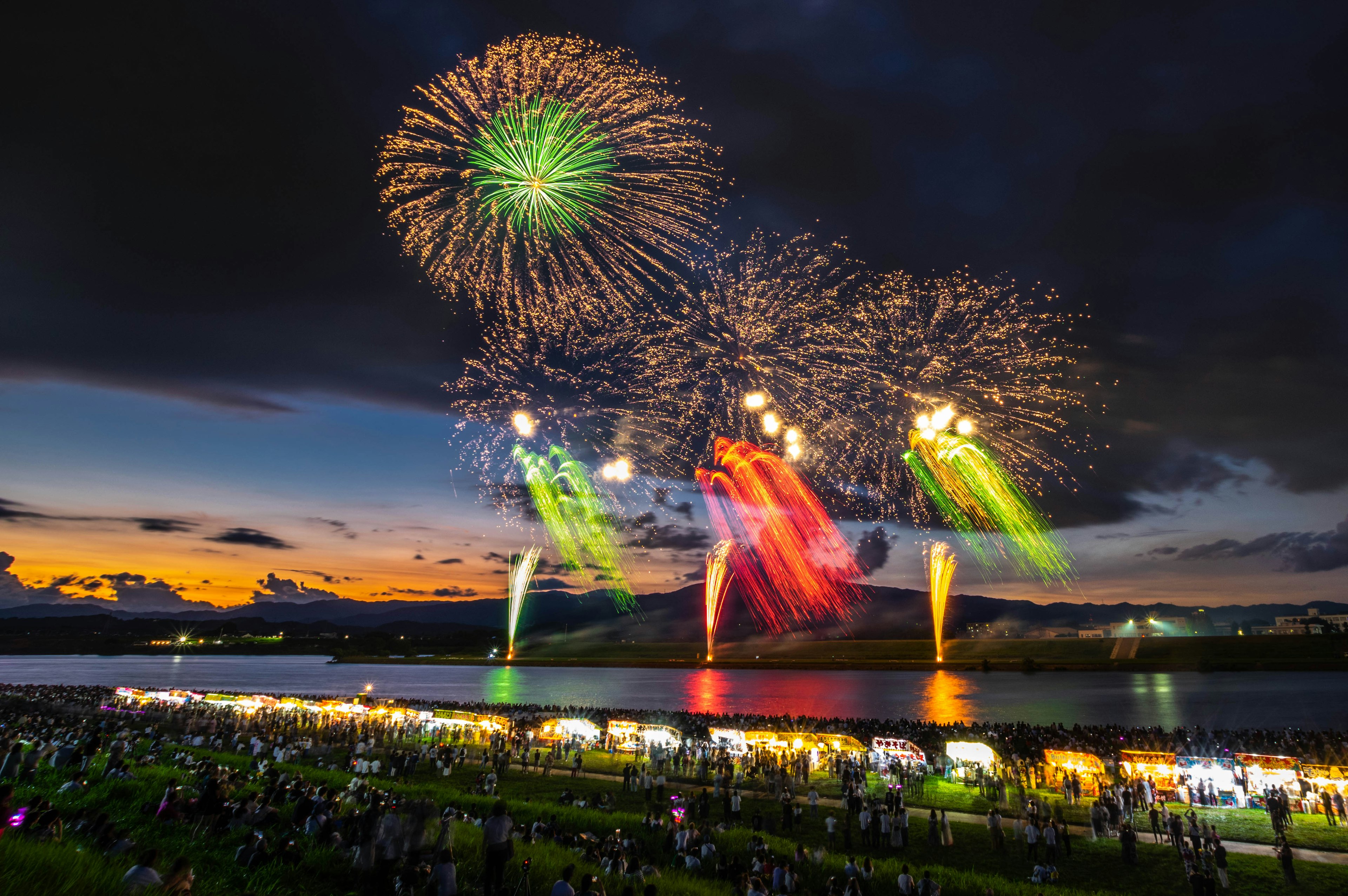 Bunte Feuerwerke erhellen den Nachthimmel über einem Fluss während eines Sommerfestes