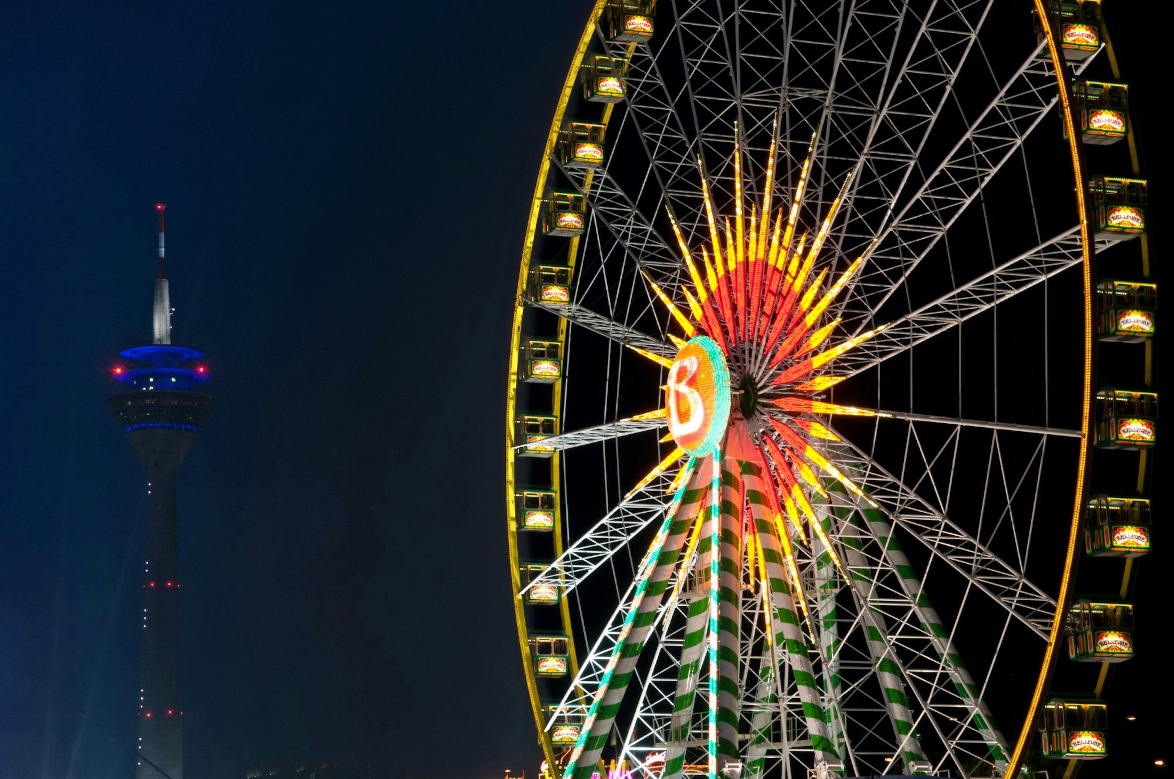 Ruota panoramica illuminata di notte con una torre sullo sfondo