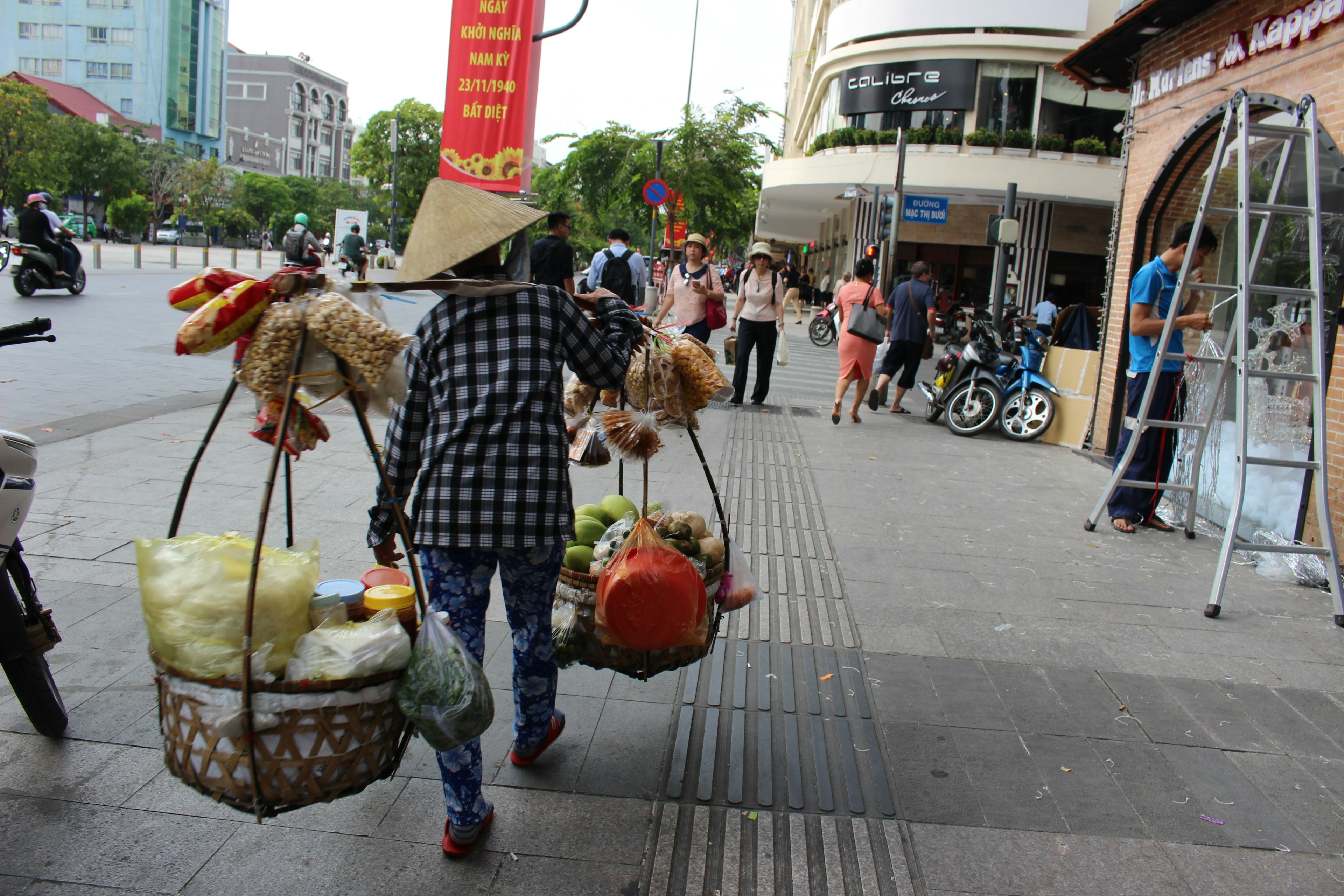 Femme portant des paniers de fruits et légumes sur ses épaules dans un coin de rue animé