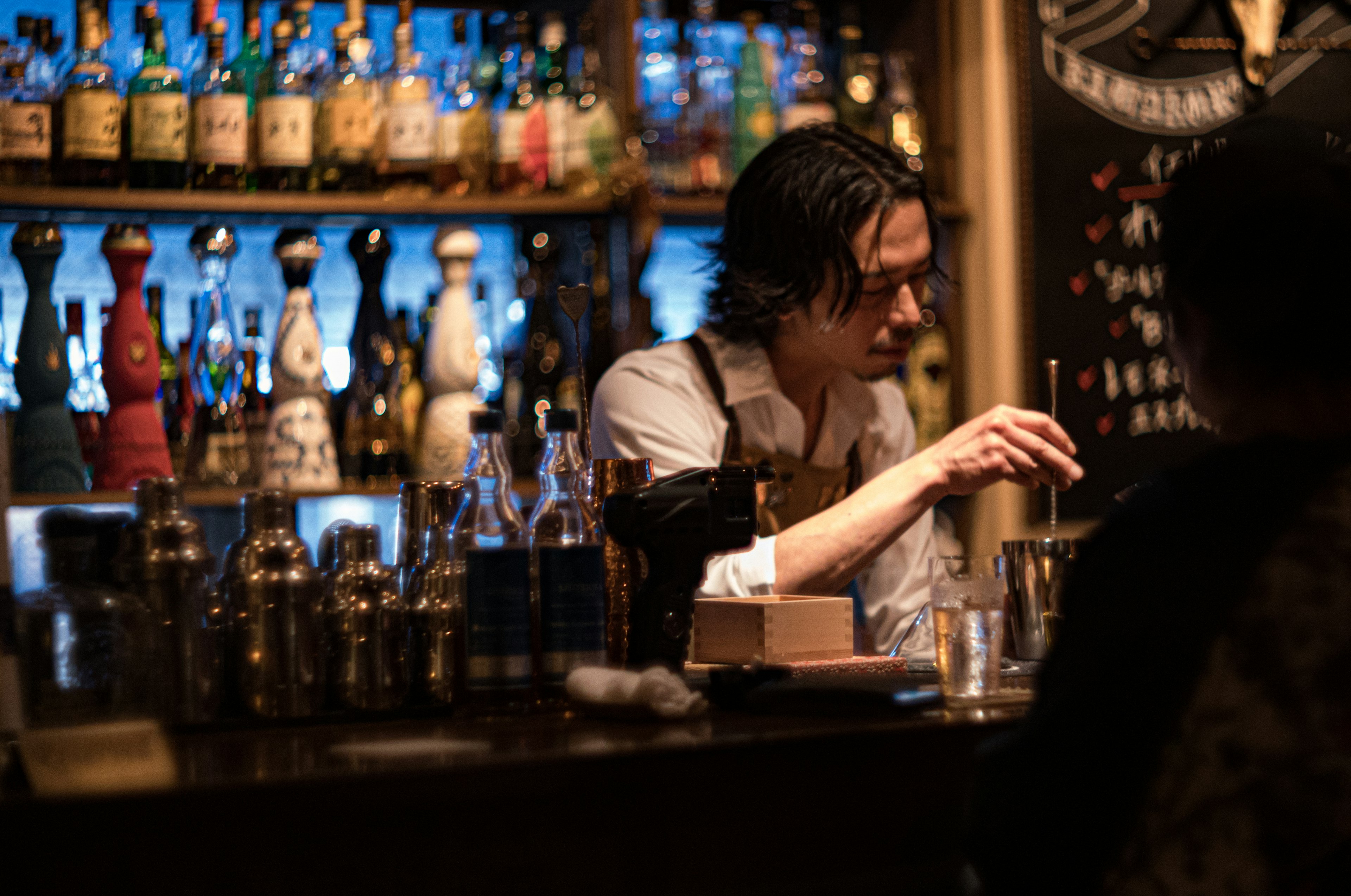 Barman preparando un cóctel con varias botellas en el bar de fondo