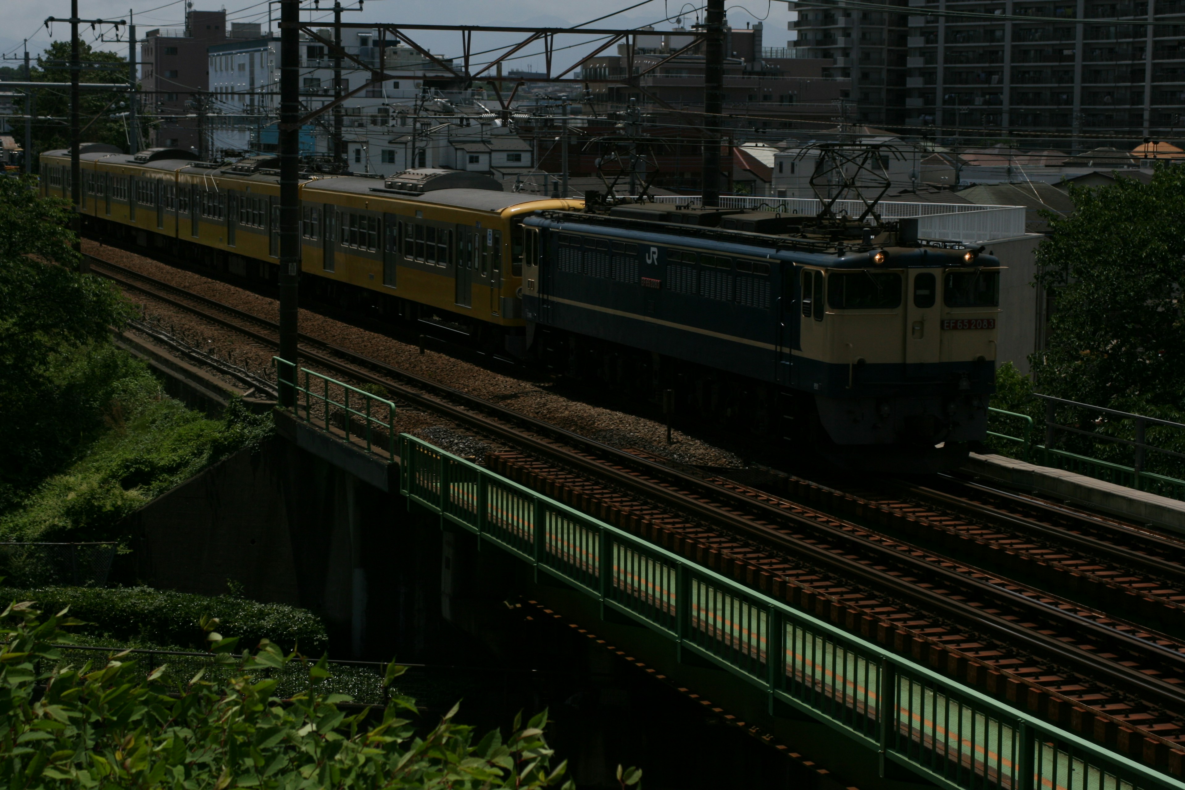 Japanese train running through green landscape featuring yellow carriages and electric locomotive