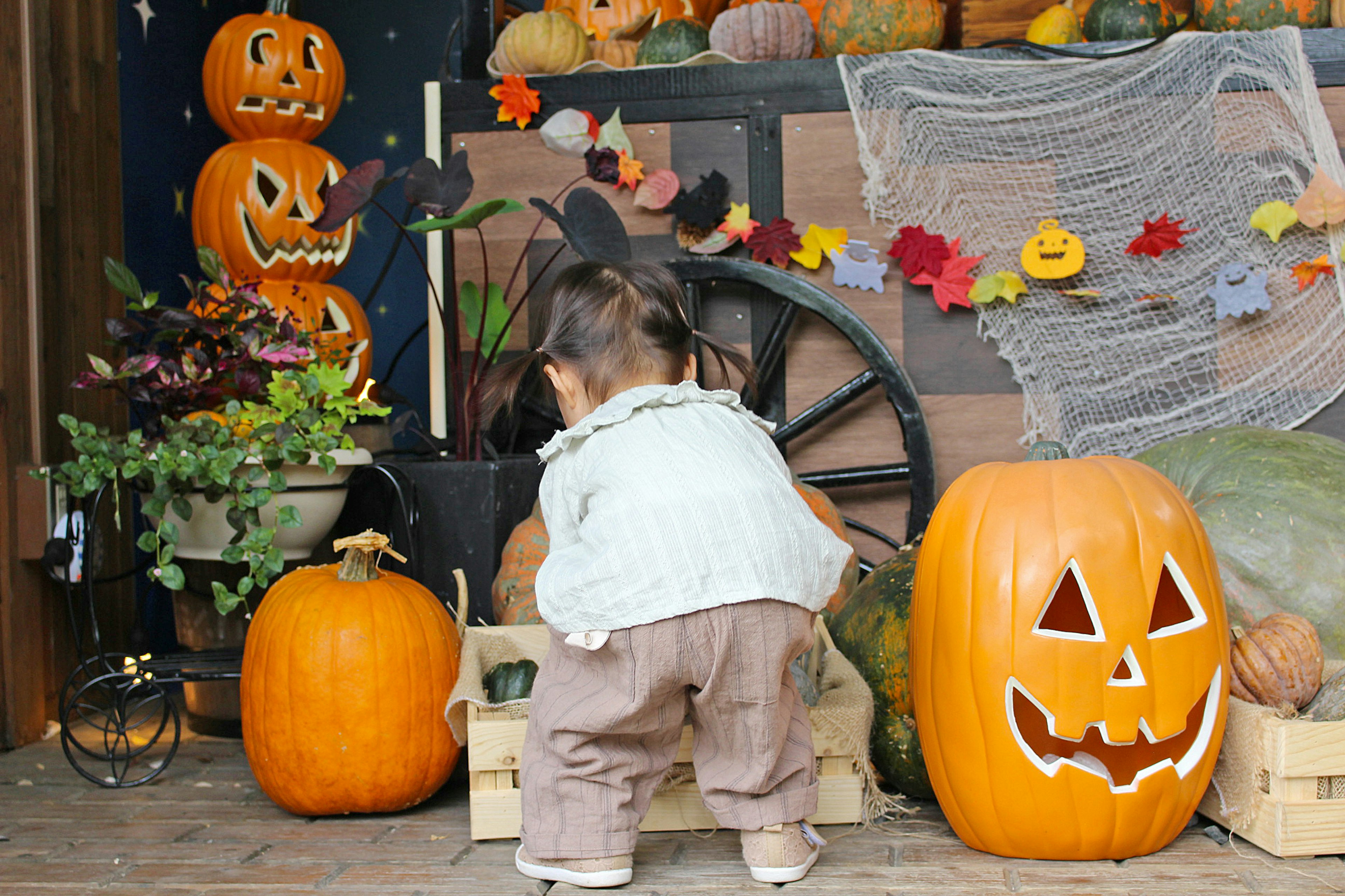 Seorang anak bermain di depan dekorasi Halloween yang menampilkan labu dan dedaunan musim gugur