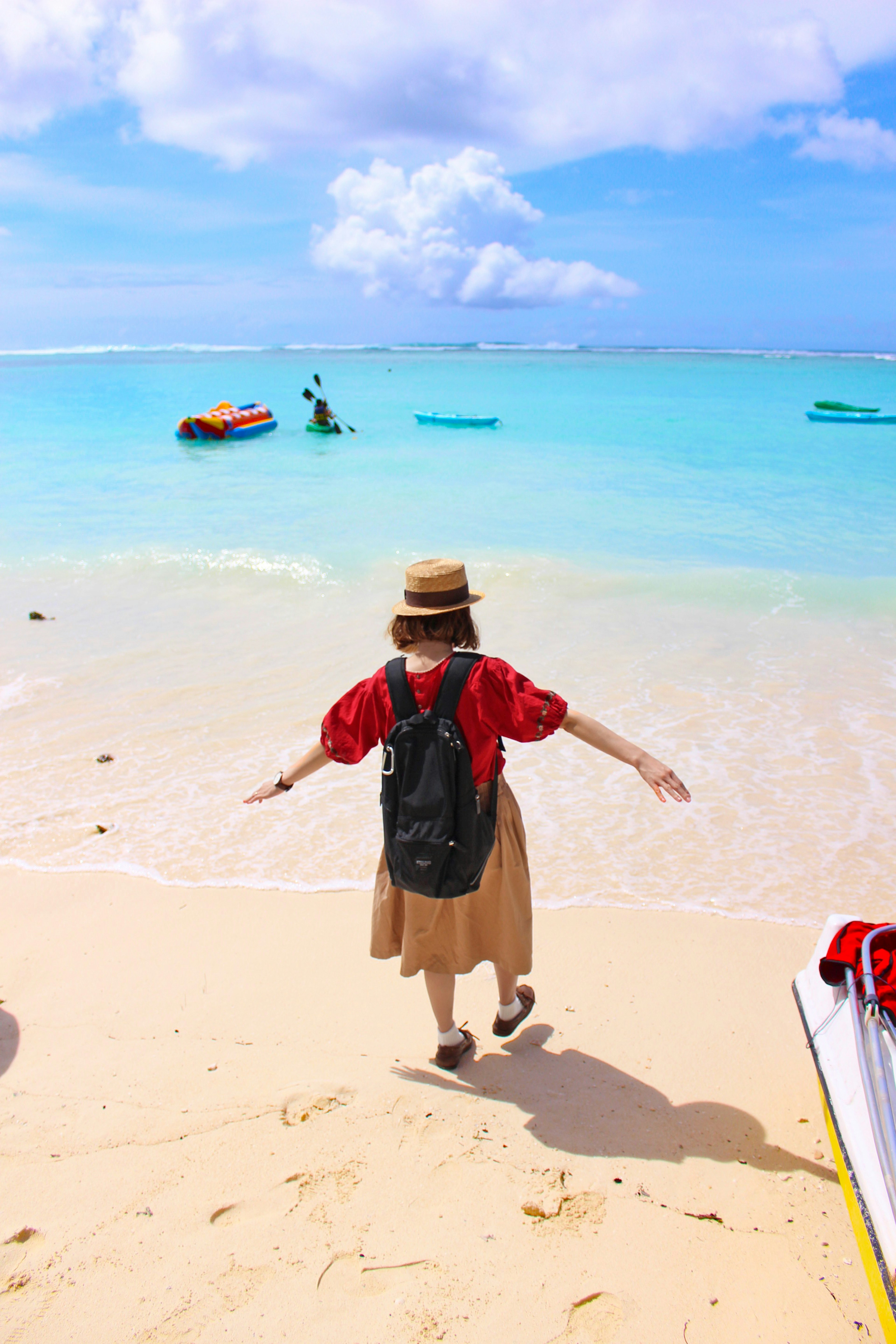 Femme profitant de la plage portant une chemise rouge et un chapeau avec un sac à dos