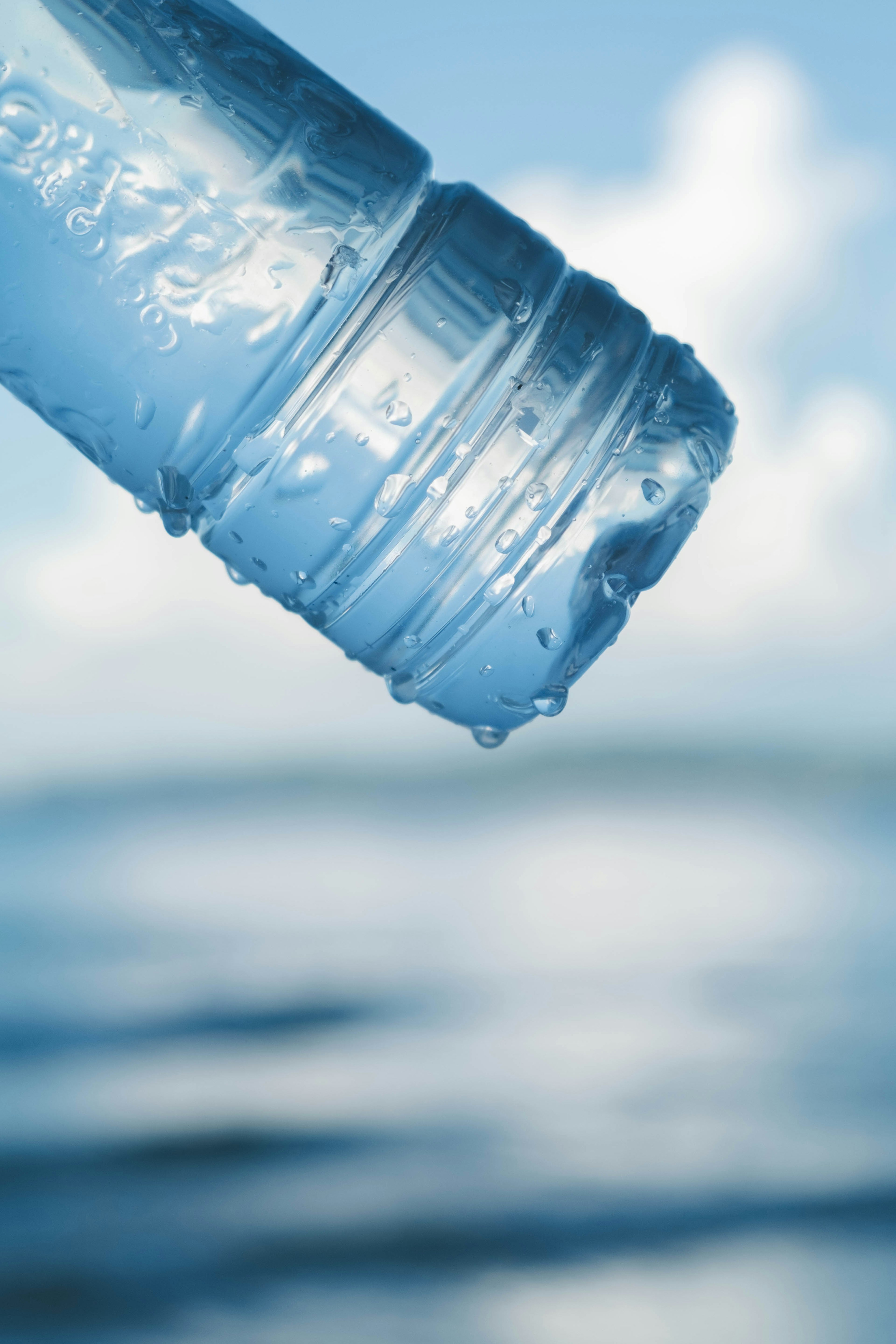 Close-up of a blue water bottle with droplets against a blurred ocean background