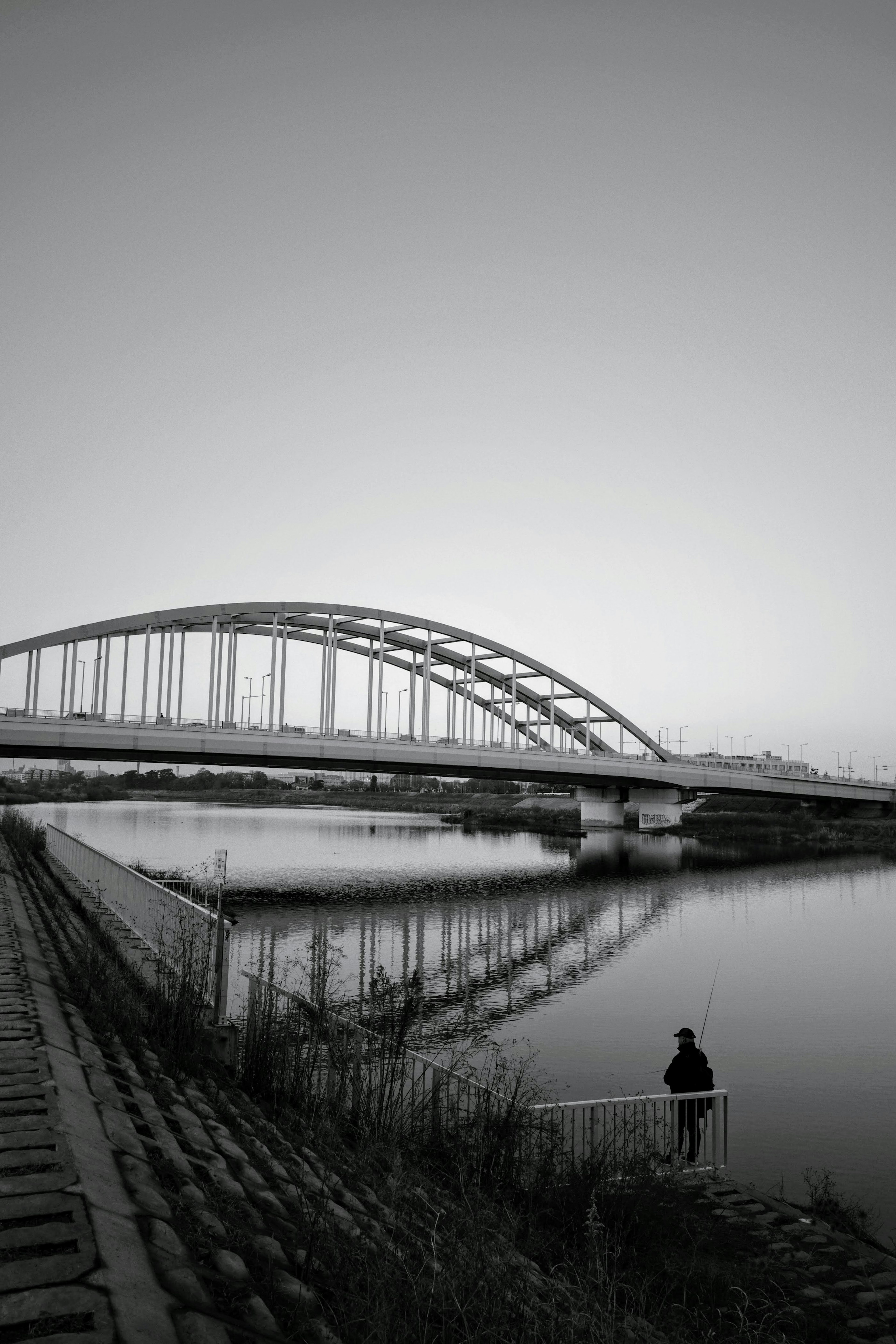 Silhouette of a person standing by a river with a black and white bridge