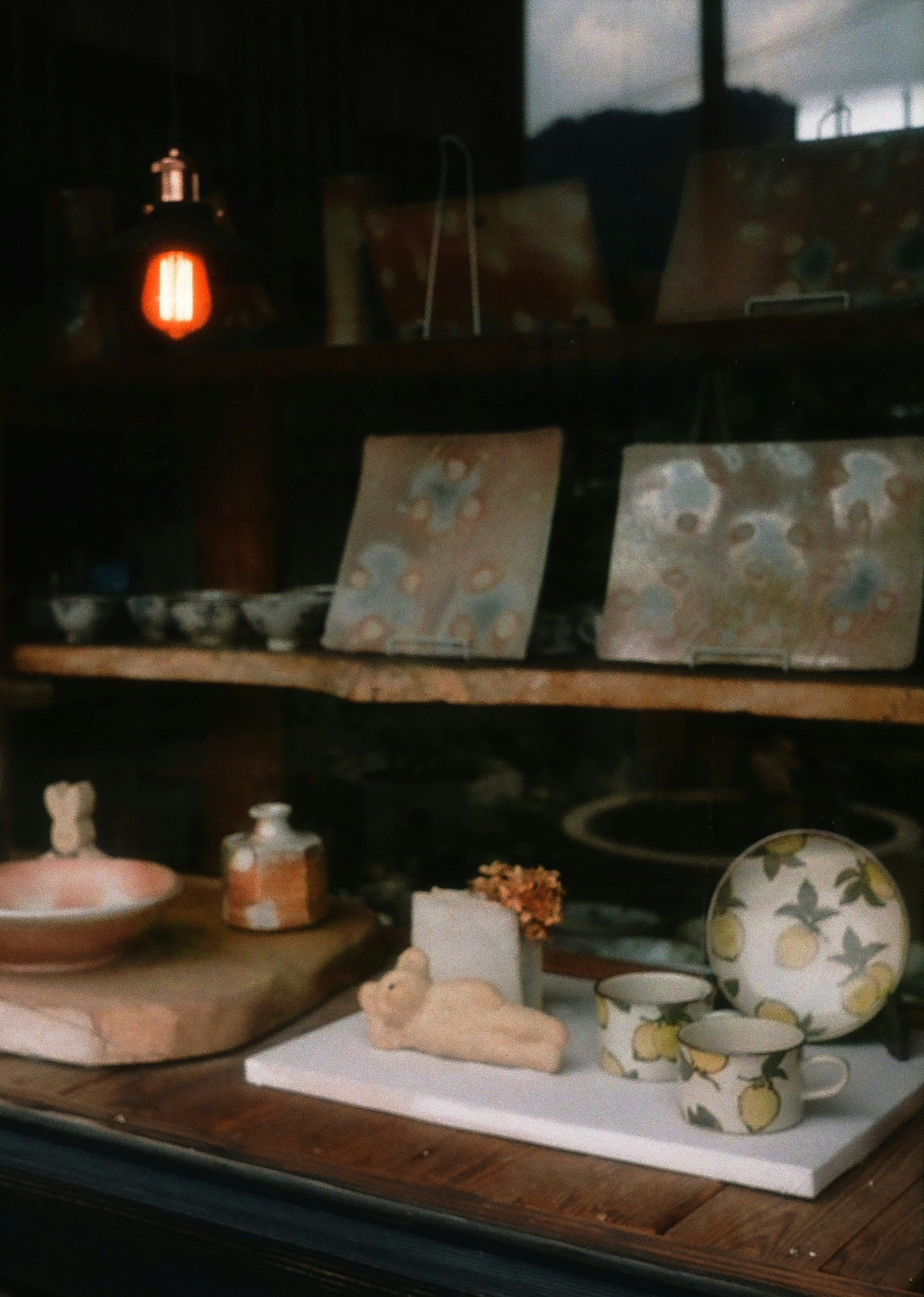 Display of pottery and plates seen through a window with a red lamp illuminating the scene