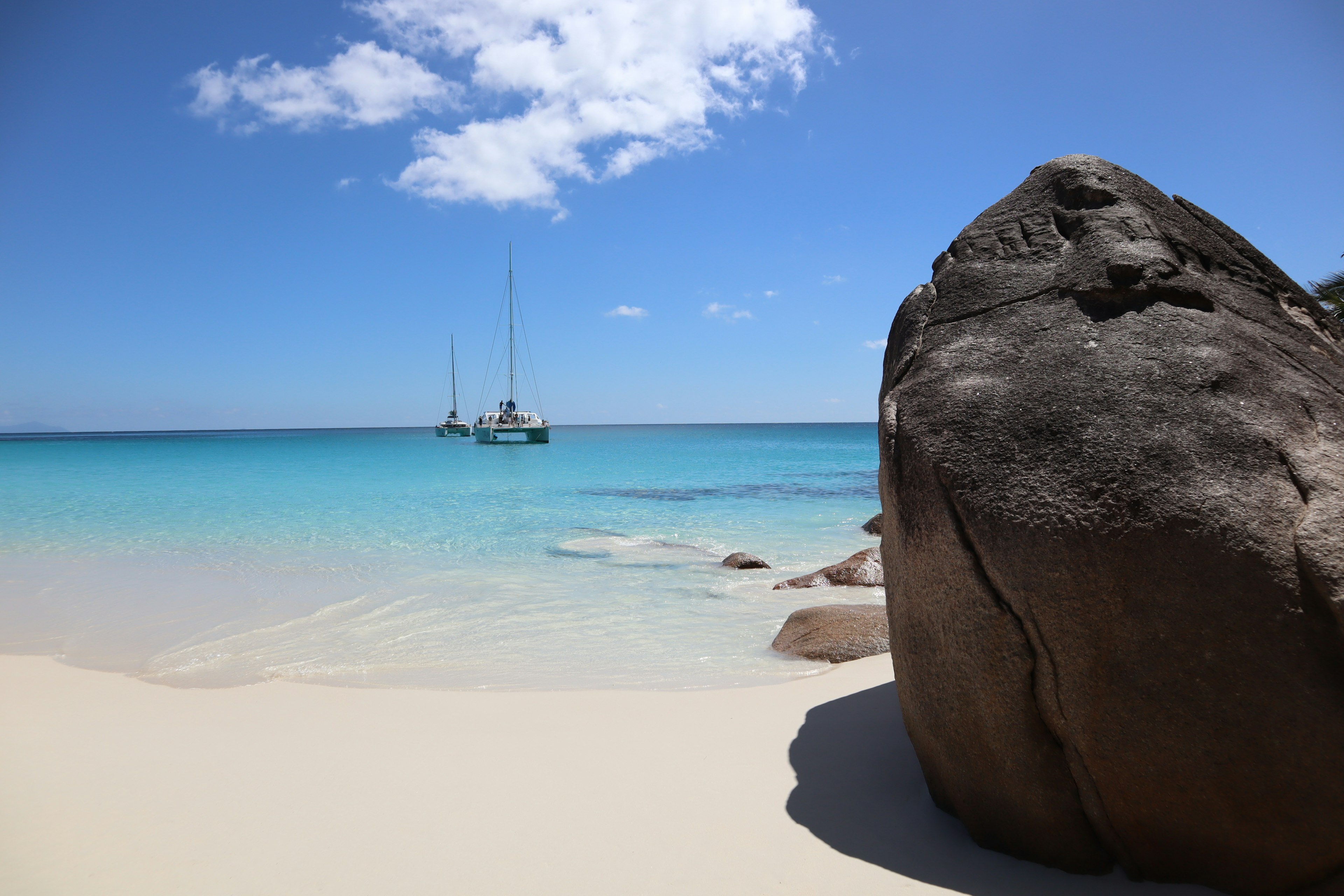 Una grande roccia su una spiaggia di sabbia bianca con acque turchesi e una barca in lontananza